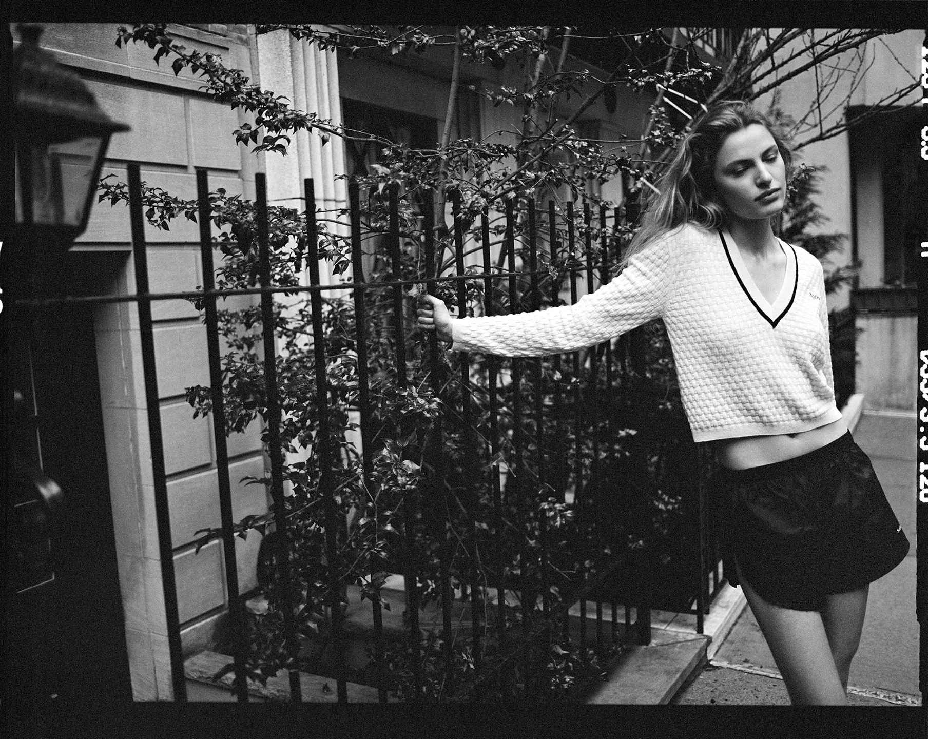 Black-and-white street portrait of Felice Nova Noordhoff in a white V-neck sweater and black shorts, photographed by Sean Thomas in New York. 
