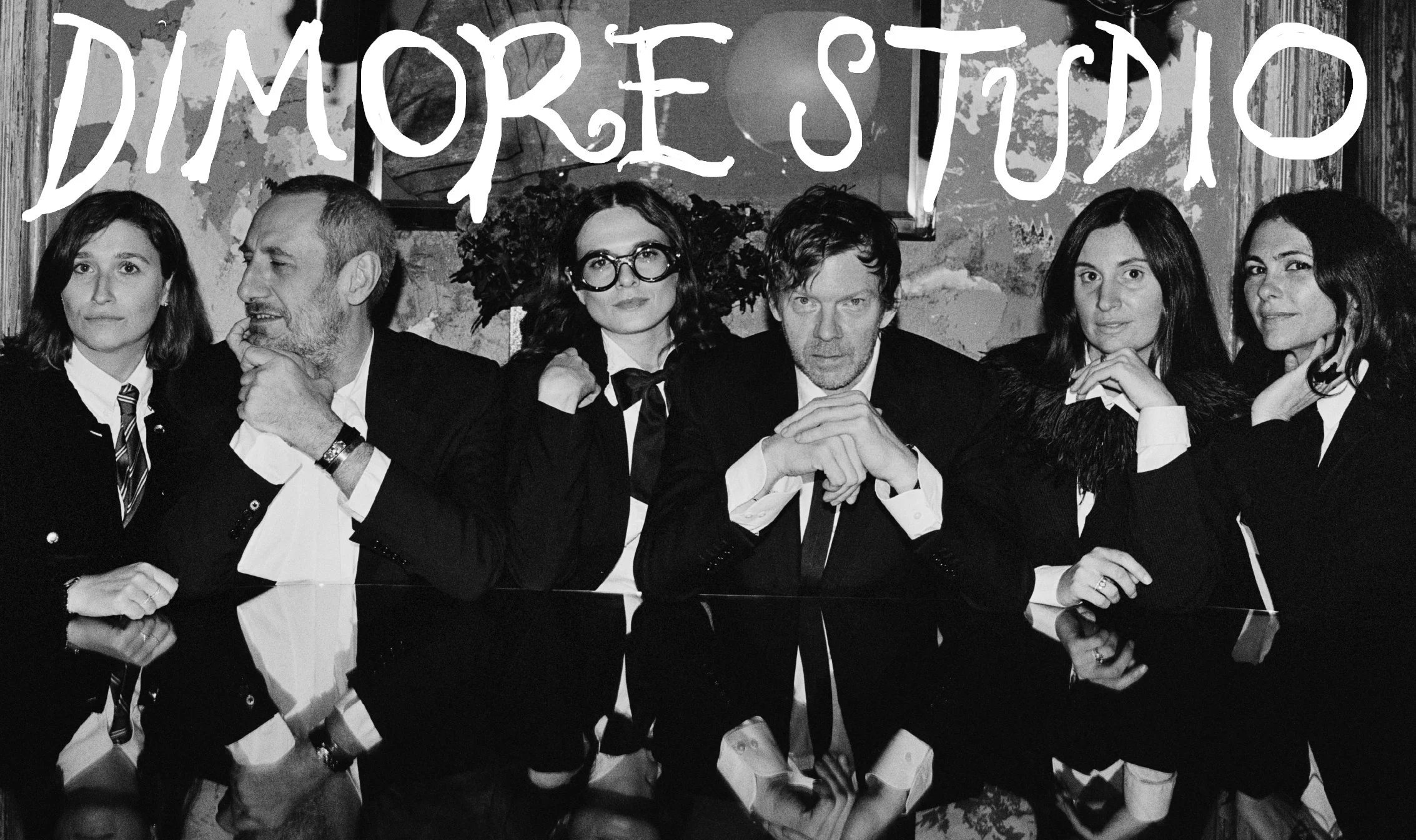  Black-and-white portrait of the Dimore Studio team seated behind a reflective table in Milan, photographed by Sean Thomas for Door’s “People Make Salone Vol. 2.” 