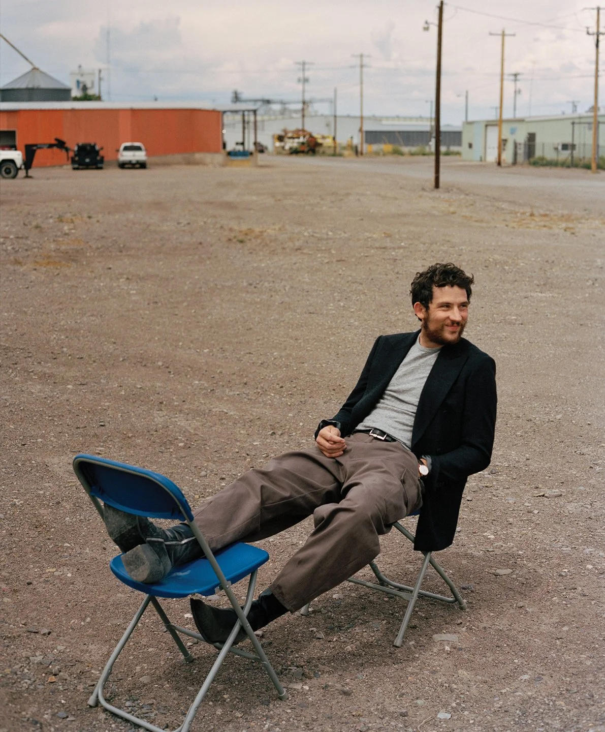  Josh O’Connor reclining across folding chairs in an industrial lot in Monte Vista, Colorado, photographed by Sean Thomas for WSJ. Magazine. 
