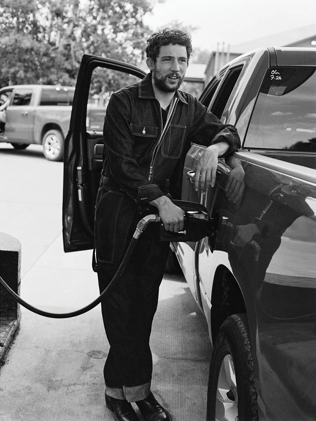  Black-and-white portrait of Josh O’Connor fueling a pickup truck in dark workwear, photographed by Sean Thomas for WSJ. Magazine in Colorado. 