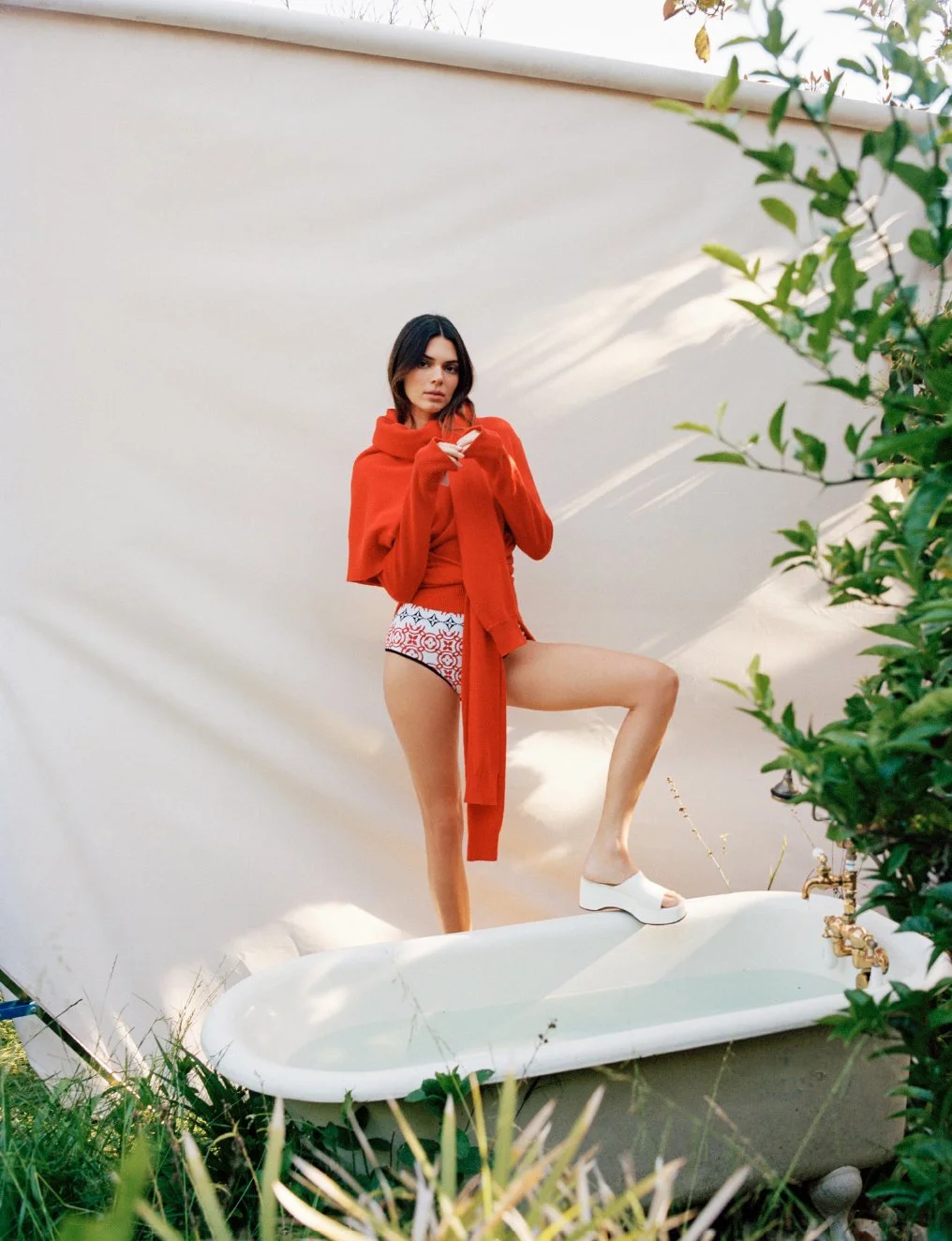  Kendall Jenner standing in an outdoor clawfoot bathtub in a red jacket and patterned swimwear, photographed by Sean Thomas in Laurel Canyon for WSJ. Magazine. 