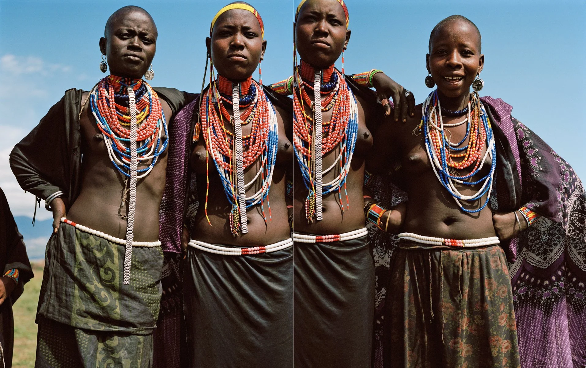  Group portrait of four Ethiopian women beneath a blue sky, wearing layered beaded jewelry and patterned skirts, photographed by Sean Thomas for Holiday Magazine. 