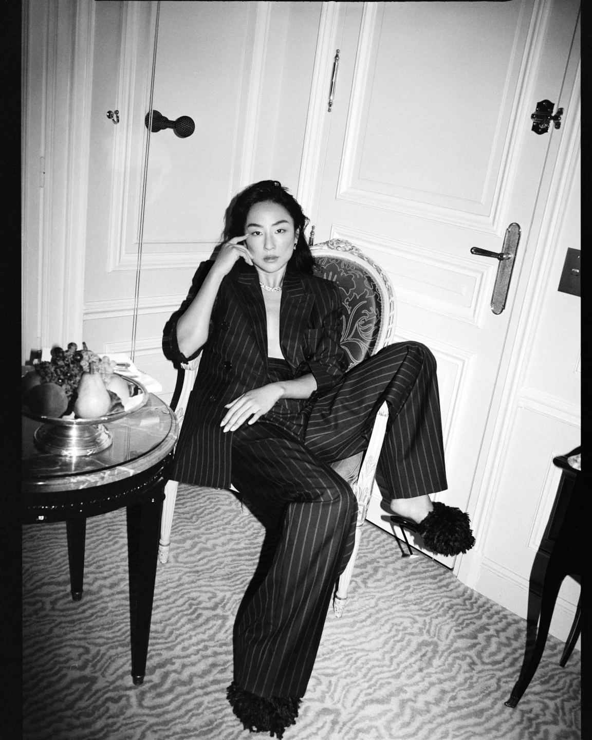  Black-and-white portrait of Greta Lee in a pinstripe suit, photographed by Sean Thomas for Sotheby’s Magazine and styled by Geraldine Saglio. 