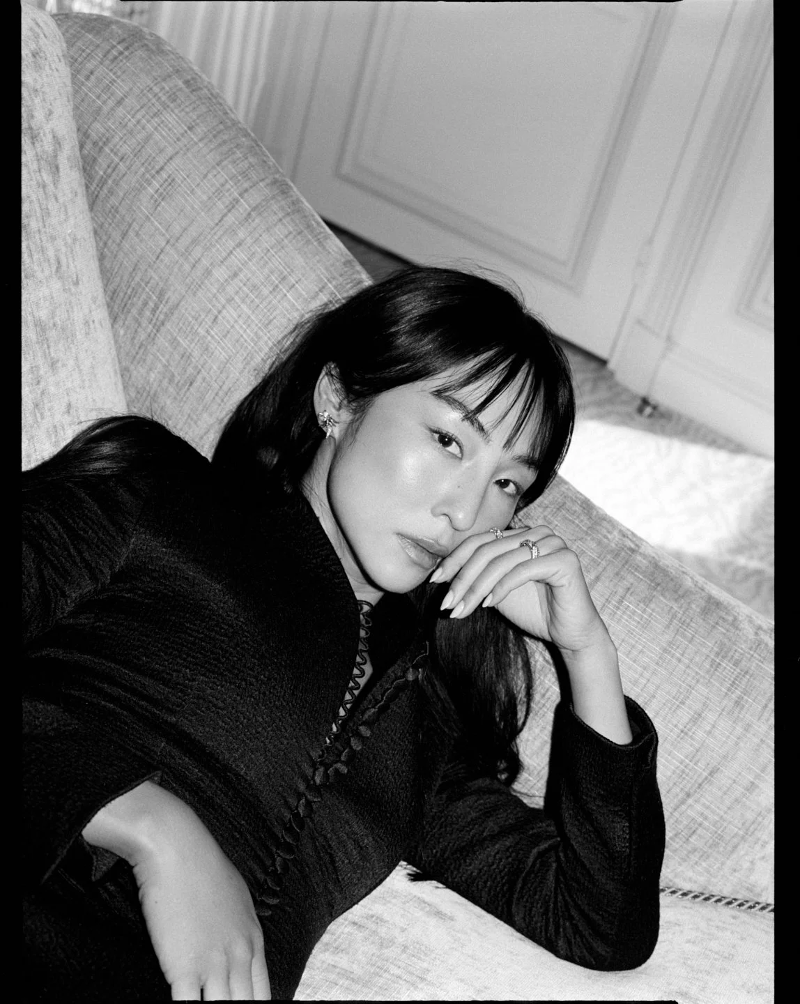  Black-and-white portrait of Greta Lee reclining in a black dress and jewelry, photographed by Sean Thomas for Sotheby’s Magazine and styled by Geraldine Saglio. 