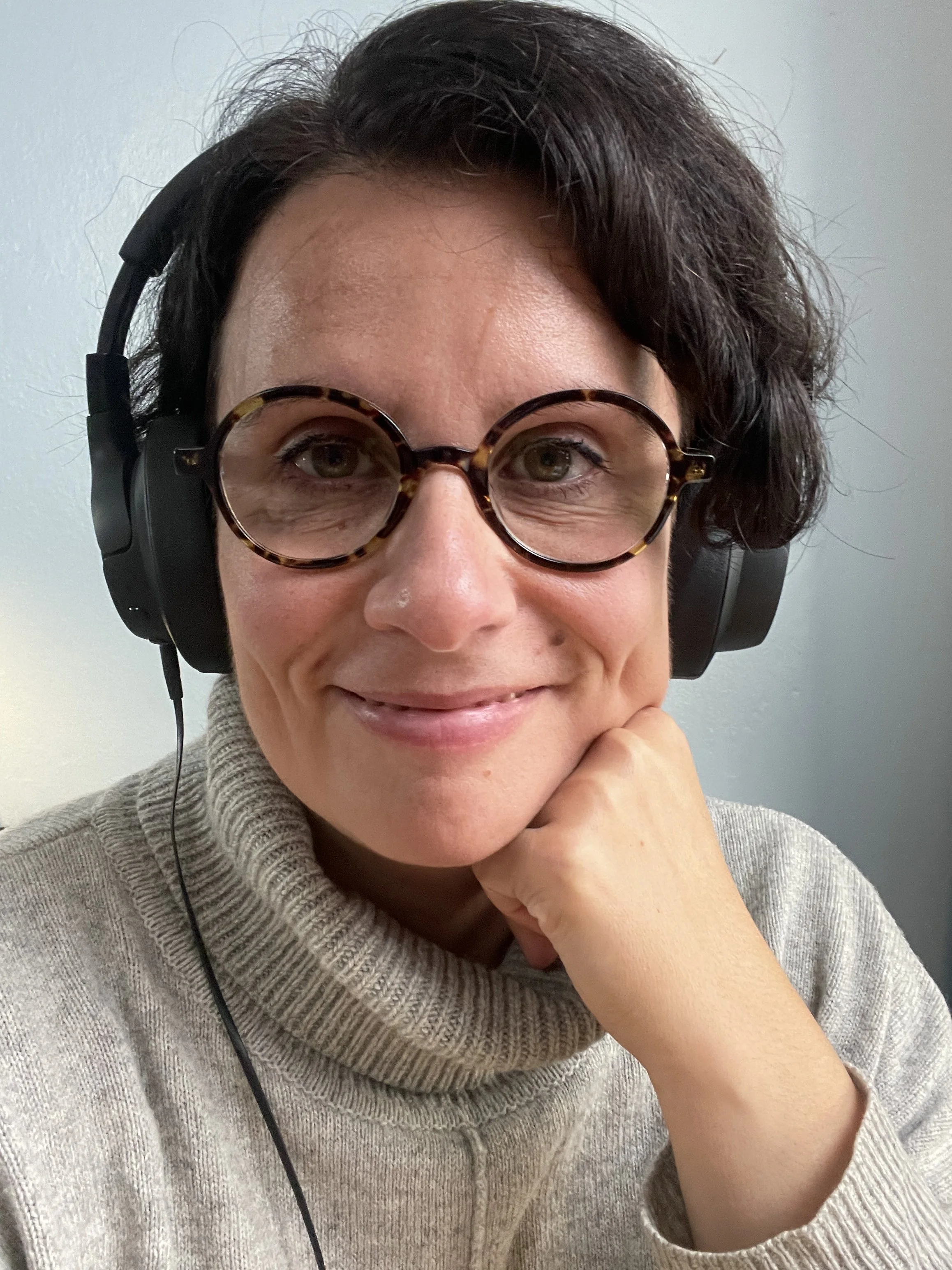 Hannele Korhonen. A woman with short dark hair and glasses looking at the camera, wearing headphones and a beige turtleneck sweater.