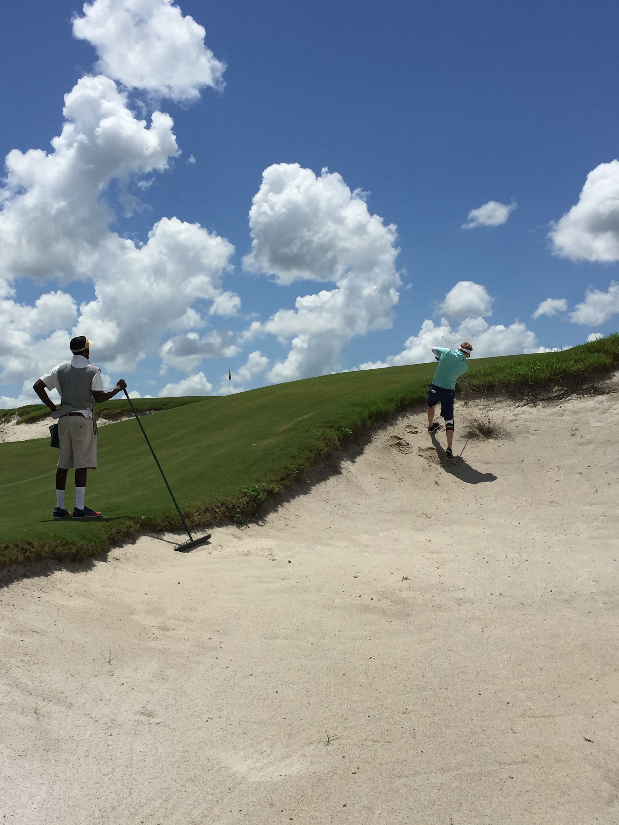 Cameron, my fiancé, tears his way out of a steep bunker on Blue with our trusty caddie Nick watching.