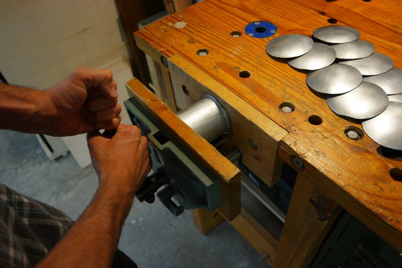  Then a great trick: by squeezing the cup extremely hard in a wood vice, the rim is both flattened and forced around until it begin to roll over on itself. 