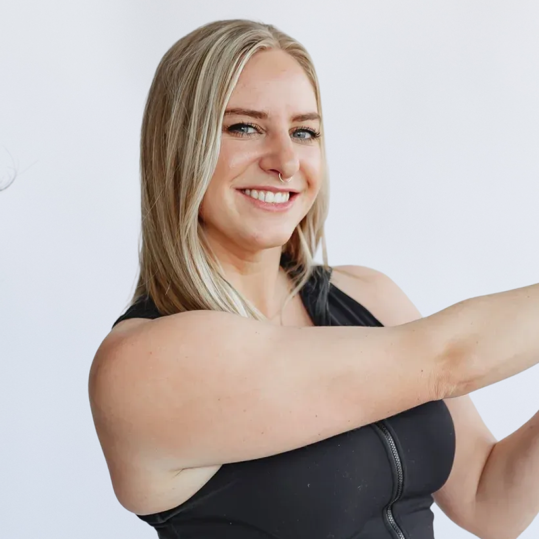 Smiling blonde woman in athletic wear stretching or exercising against a plain white background.