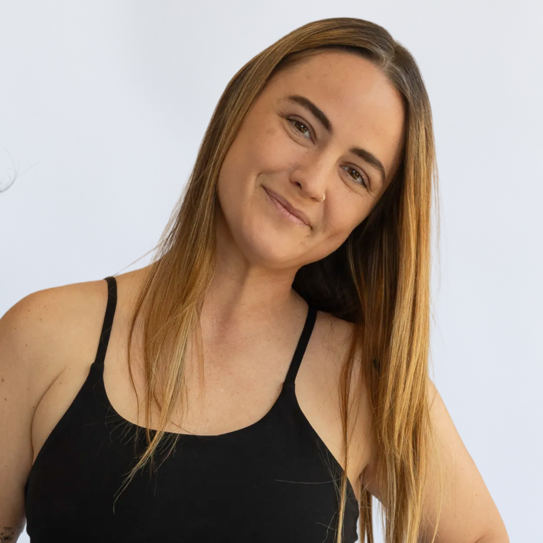 Young woman with long blonde hair, wearing a black top and black jacket, smiling against a plain white background.