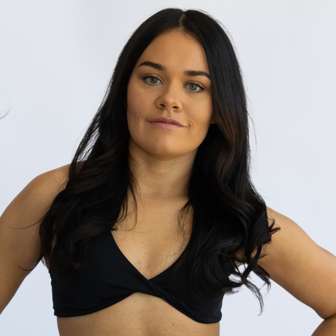 Woman with long dark hair in a black crop top against a plain white background.