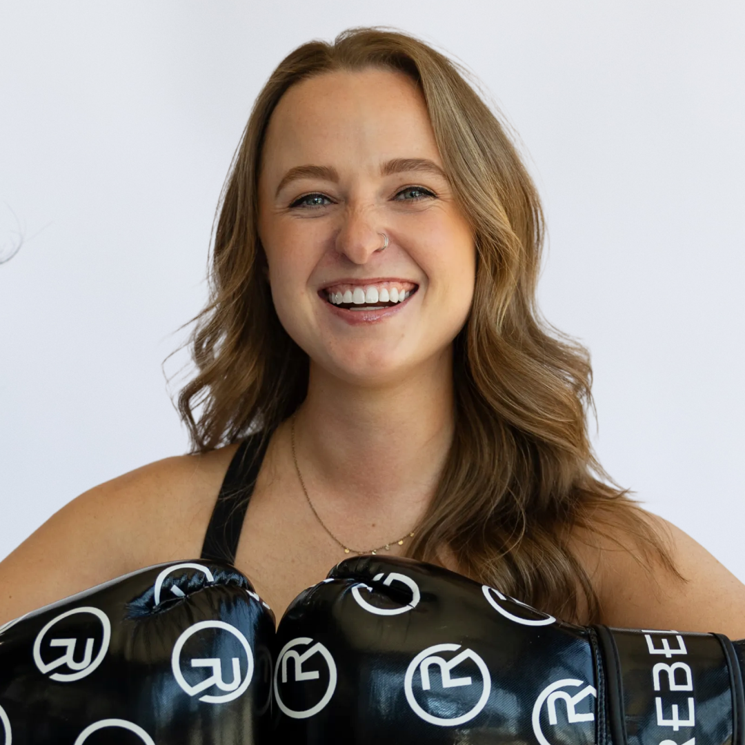 A smiling young woman wearing boxing gloves with a Reebok logo.