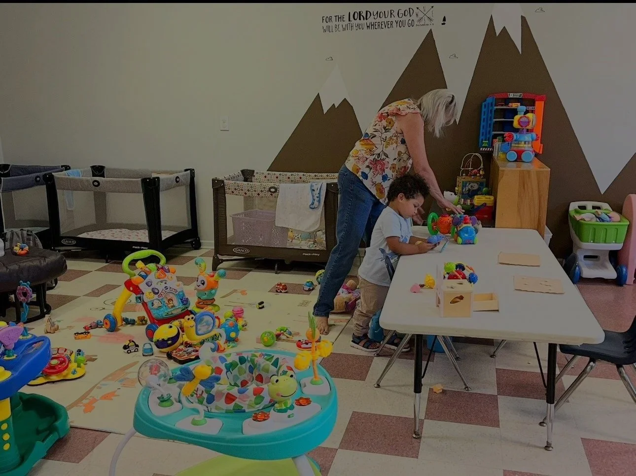 A woman and a young boy playing with colorful toys and blocks at a table in a children's playroom decorated with mountain and snowcap wall art. Little Lambs at Life Church of Monroe