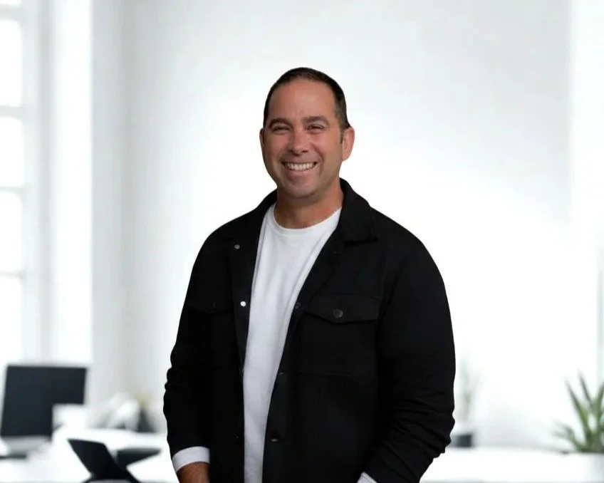 A smiling man in a yellow polo shirt standing in front of a red circular background.