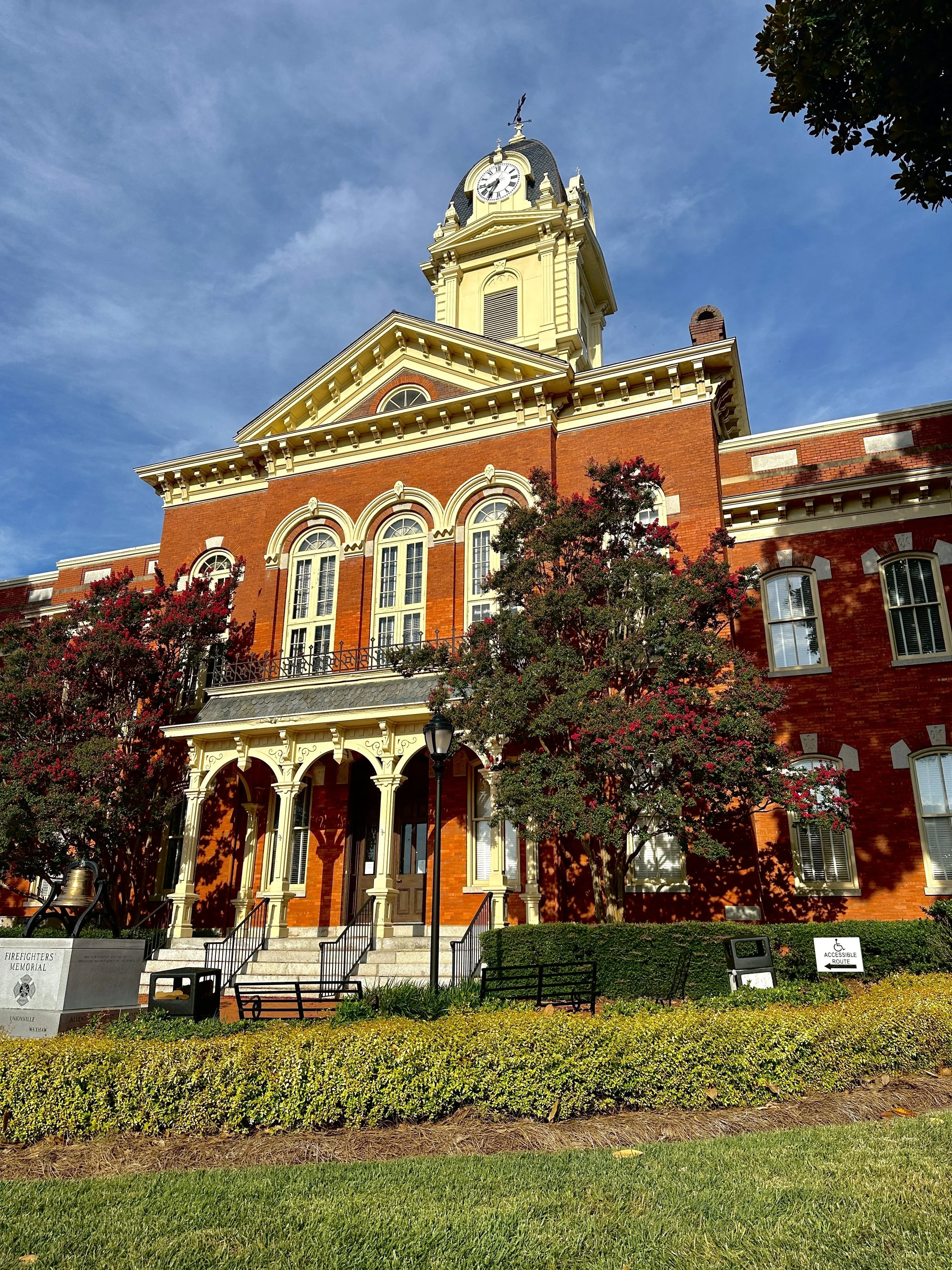 A historic brick building with a clock tower, surrounded by trees and a manicured lawn.