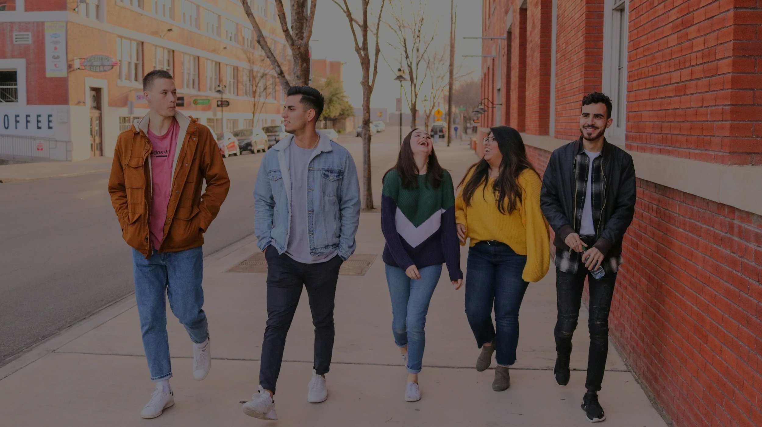 Group of five young people walking and talking on city sidewalk during daylight.
