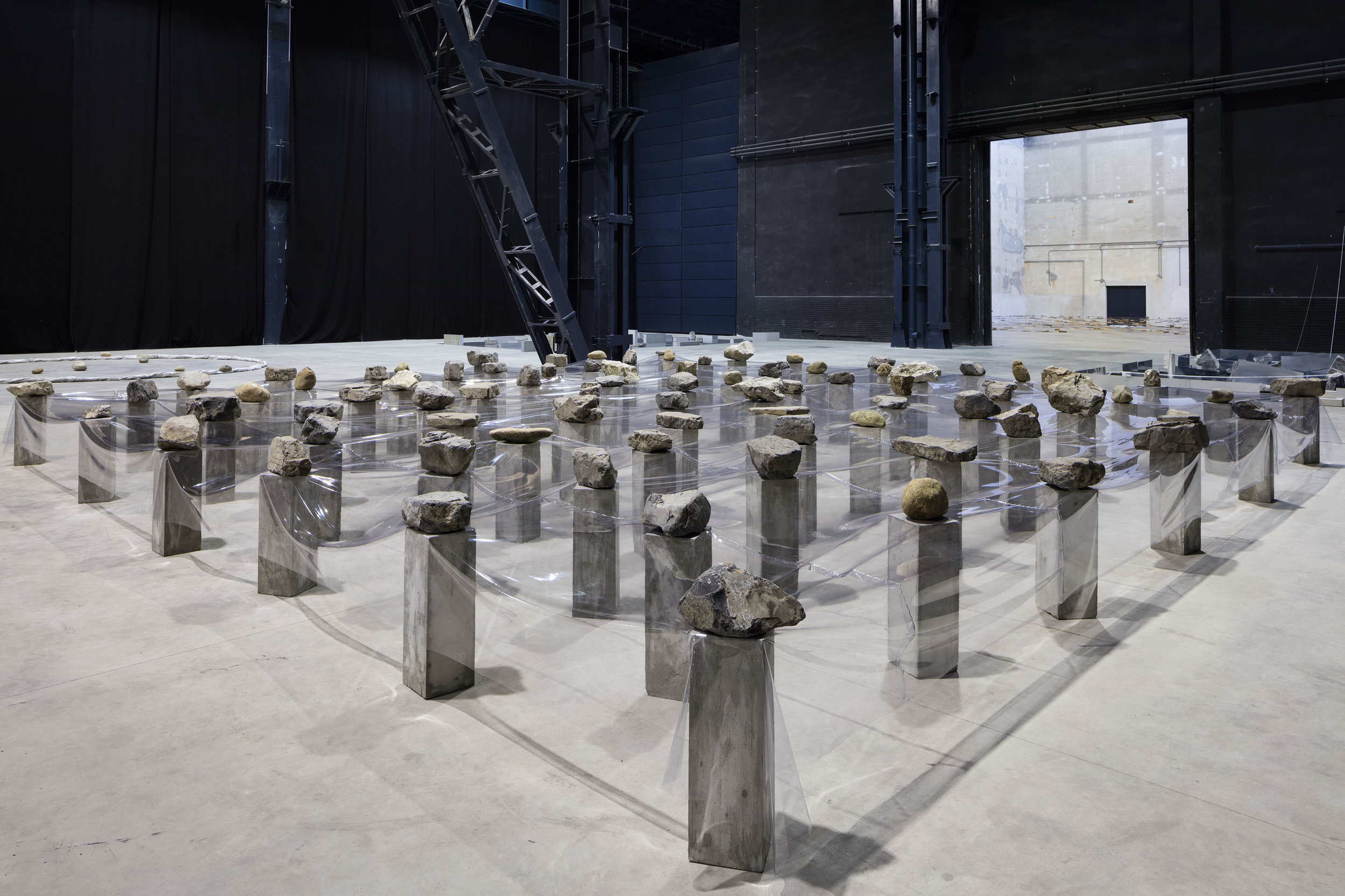 Law of Multitude , 1975/2016 多分律 ( Tabunritsu ) Plastic sheet, stone, concrete 100 x 875 x 850 cm Installation view, Kishio Suga: Situations , Pirelli HangarBicocca, Milan, 2016 Photo: Agostino Osio; Courtesy Pirelli HangarBicocca, Milan