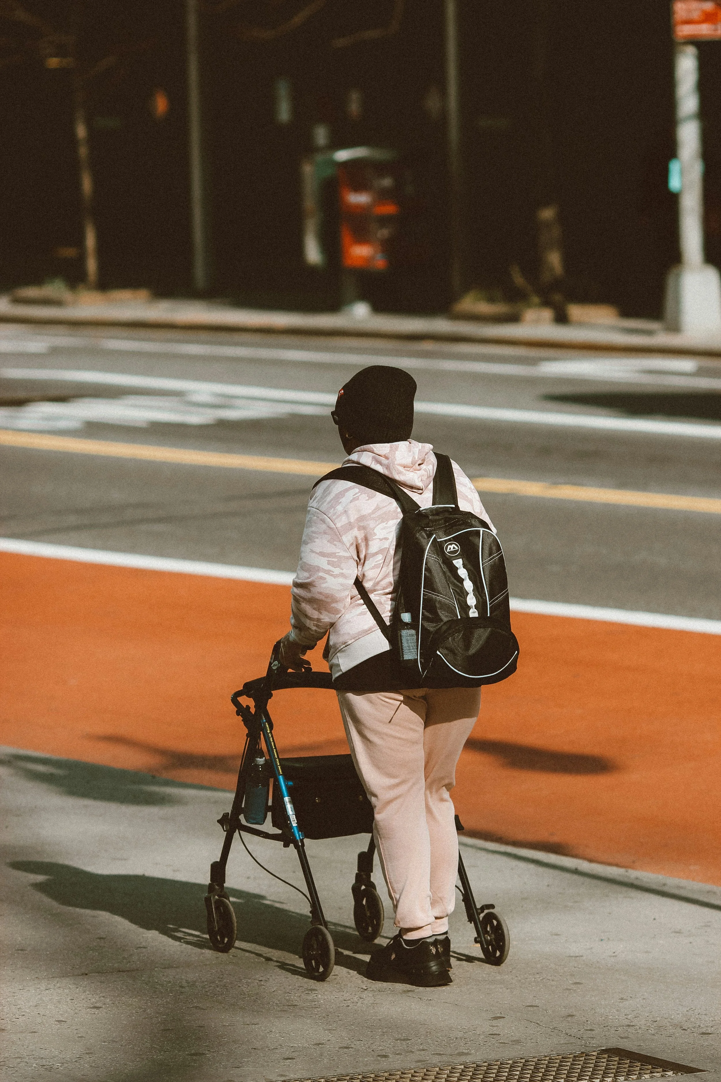 The back of a person using a rollator on a public sidewalk with the street in the background walking away. Represents Seattle LMFT for health issues.