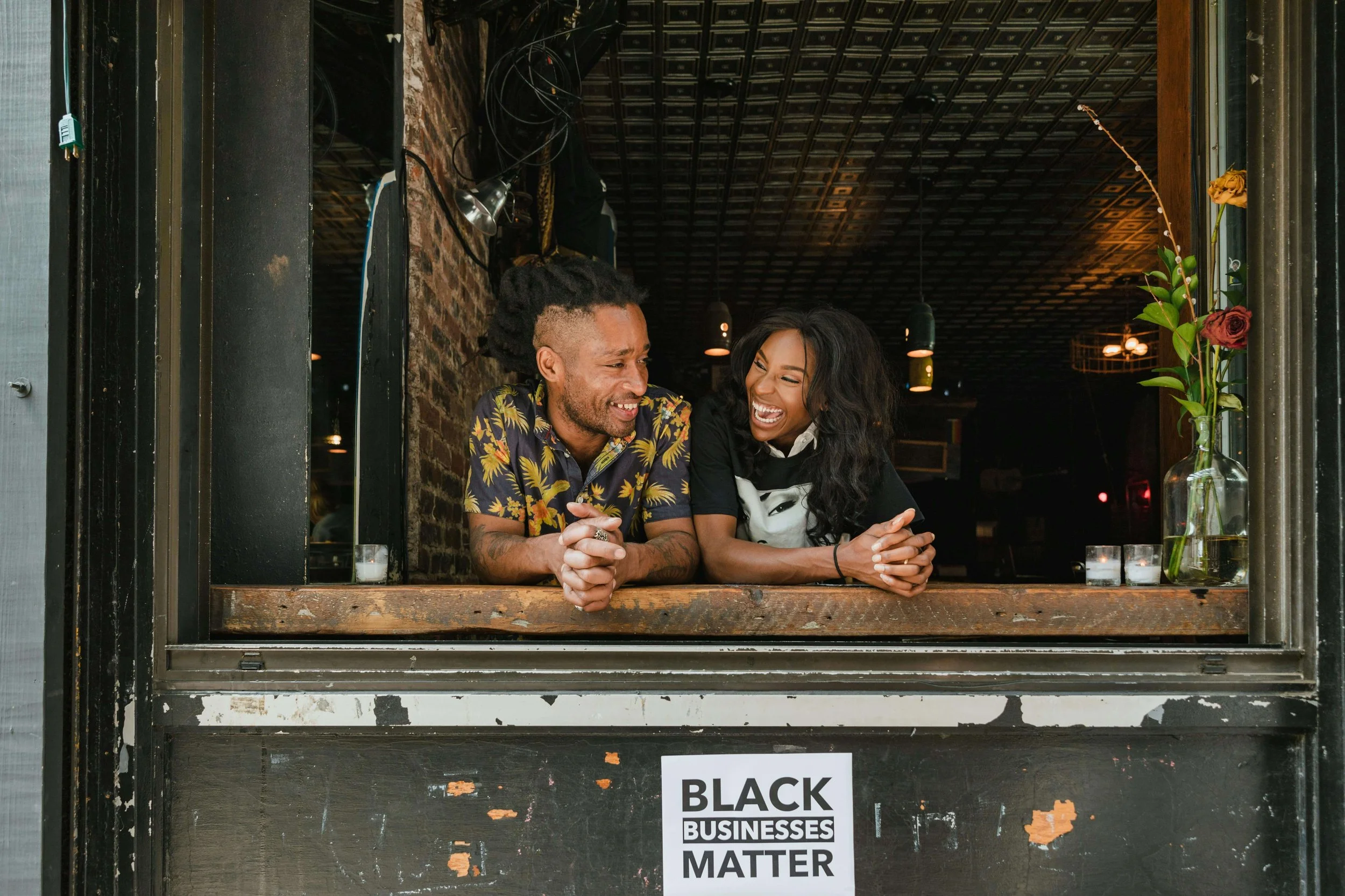 A black man and woman leaning out a window of their local business. Represents anxiety therapy in Seattle.