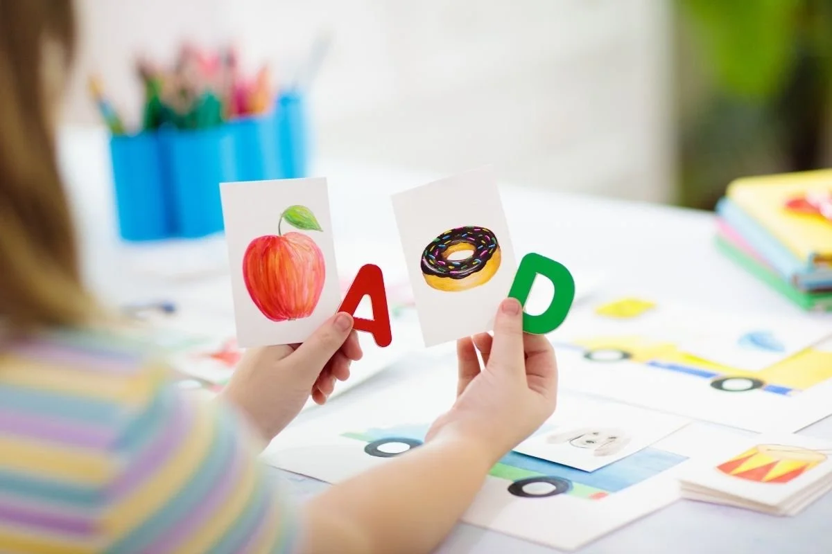 Kindergartener practicing letter sounds with alphabet picture cards as a back-to-school reading activity.