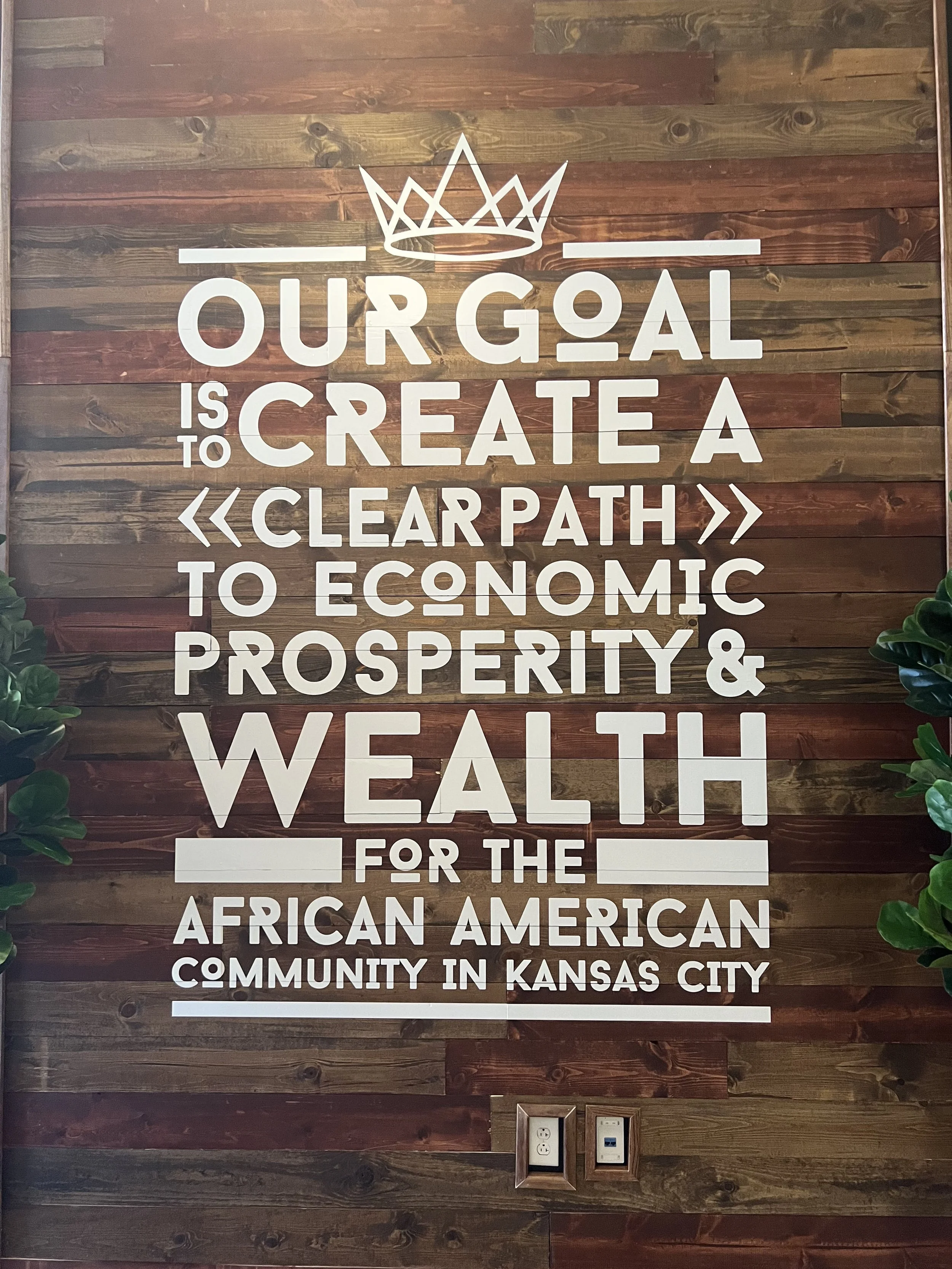 KC G.I.F.T. reclaimed wood feature wall with bold typography displaying the organization’s mission to create economic prosperity and wealth for the African American community in Kansas City.