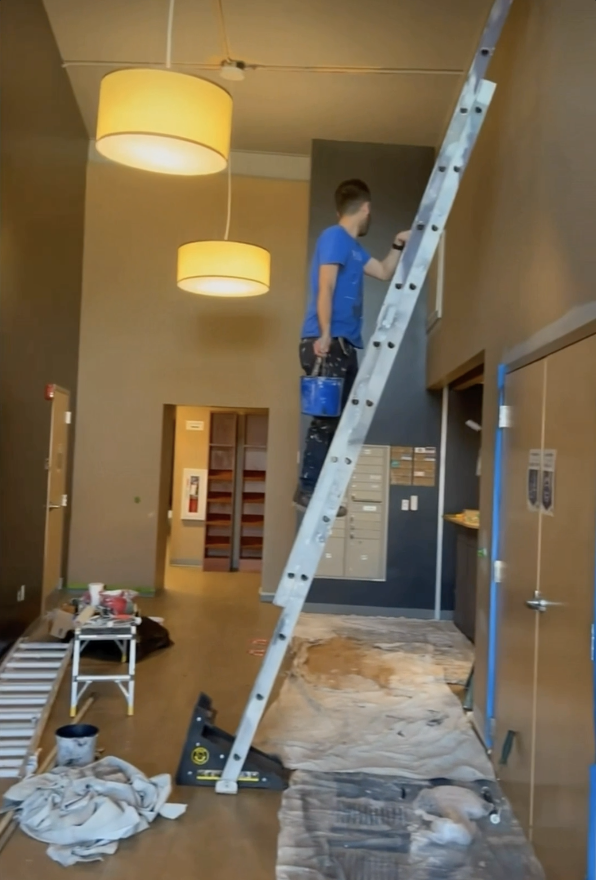 Installation phase of KC G.I.F.T. entryway transformation showing a contractor on a ladder preparing the wall, with tools, materials, and protective coverings in place during renovation.