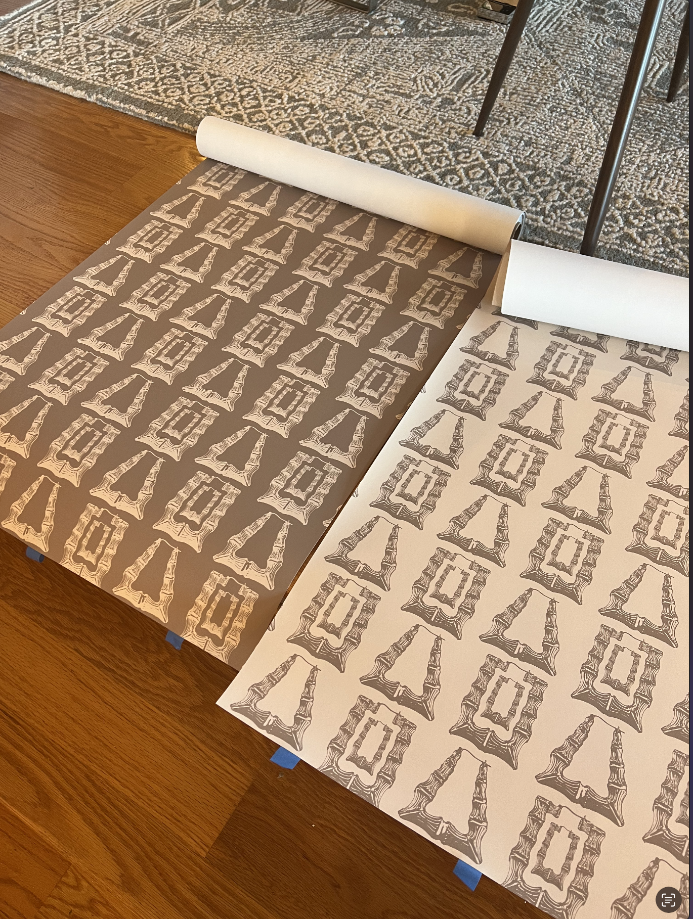Two custom wallpaper samples in inverse neutral colorways laid side by side on a hardwood floor during design development.