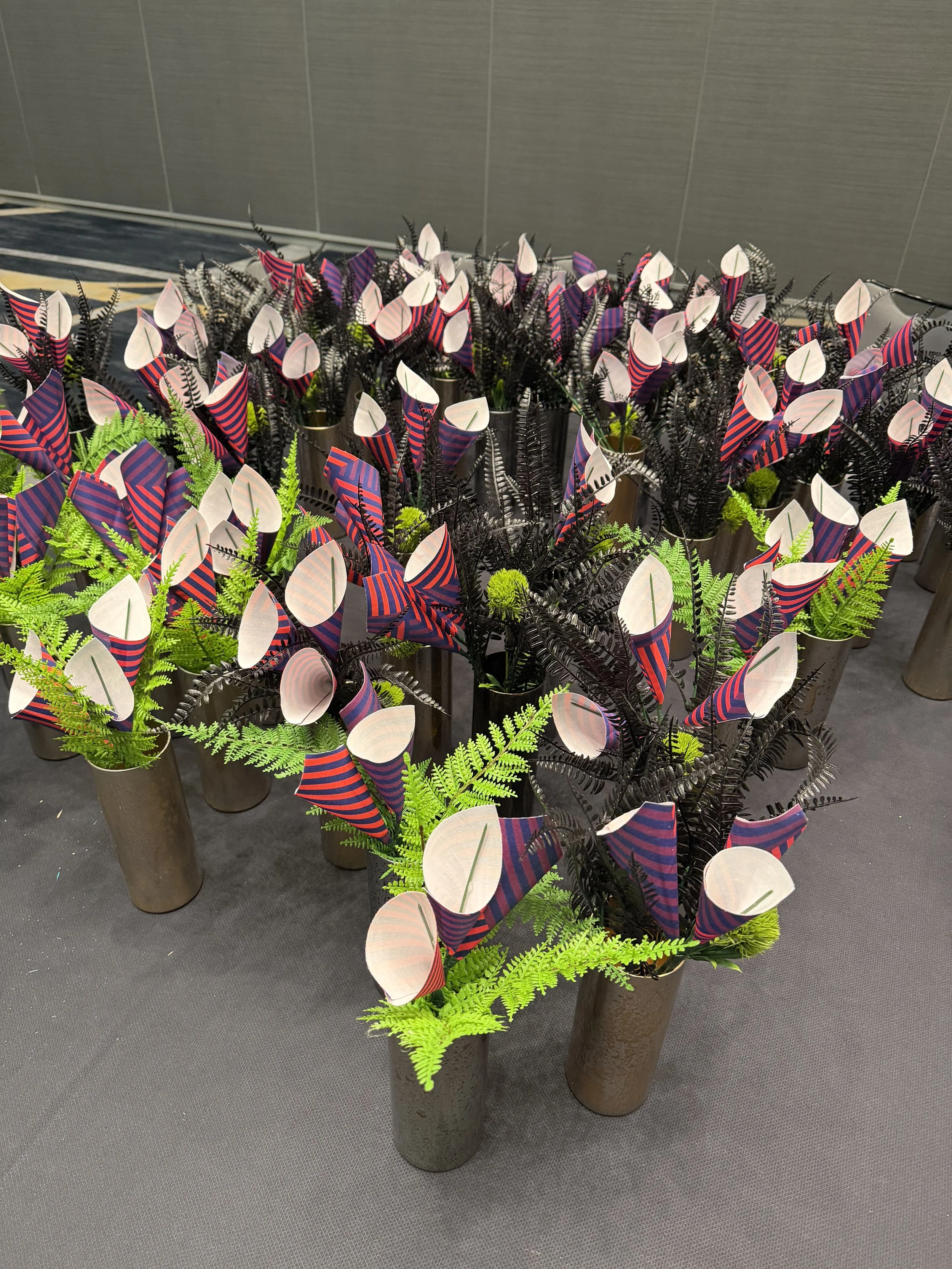 Colorful fabric flowers with black and green fern foliage arranged in tall metallic vases.