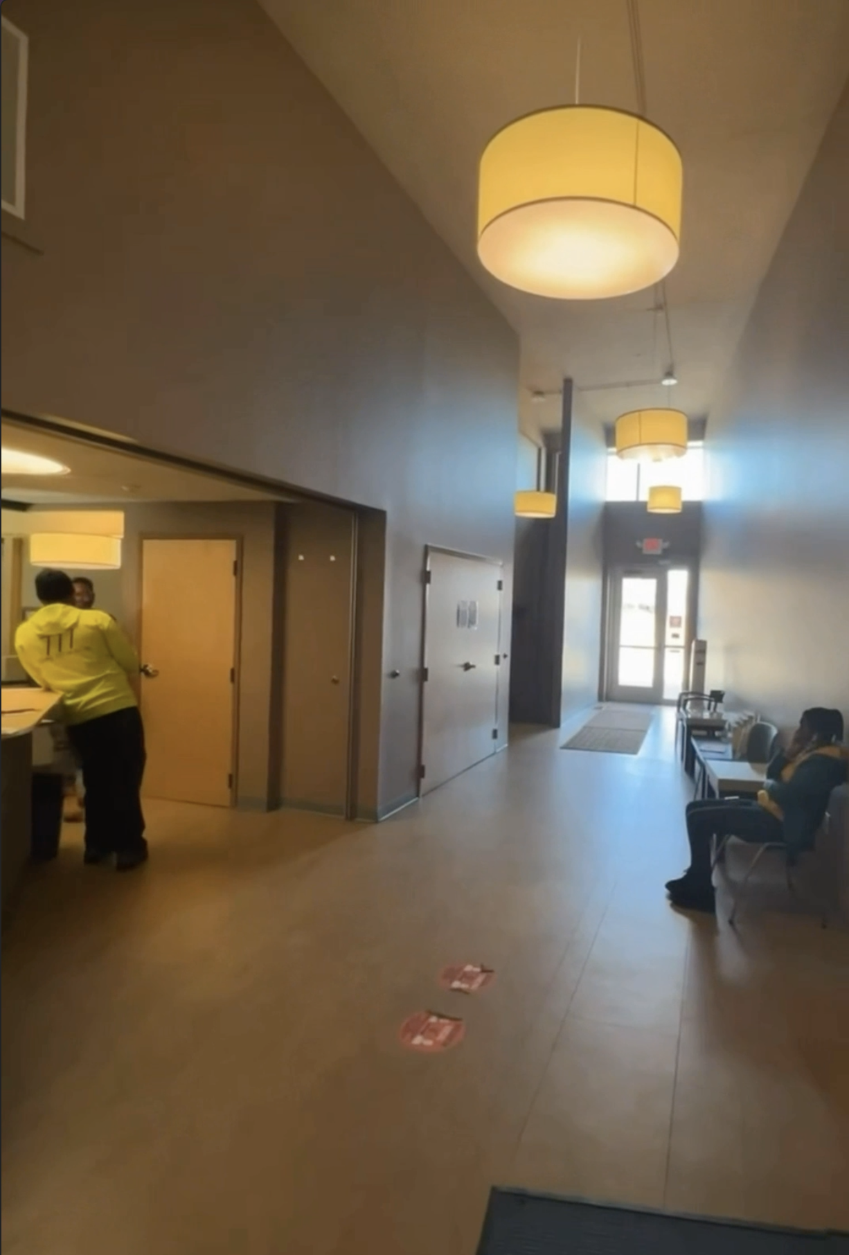 Before image of KC G.I.F.T. lobby showing a wide, neutral hallway with pendant lighting, minimal seating, and an undefined layout lacking visual identity and warmth.