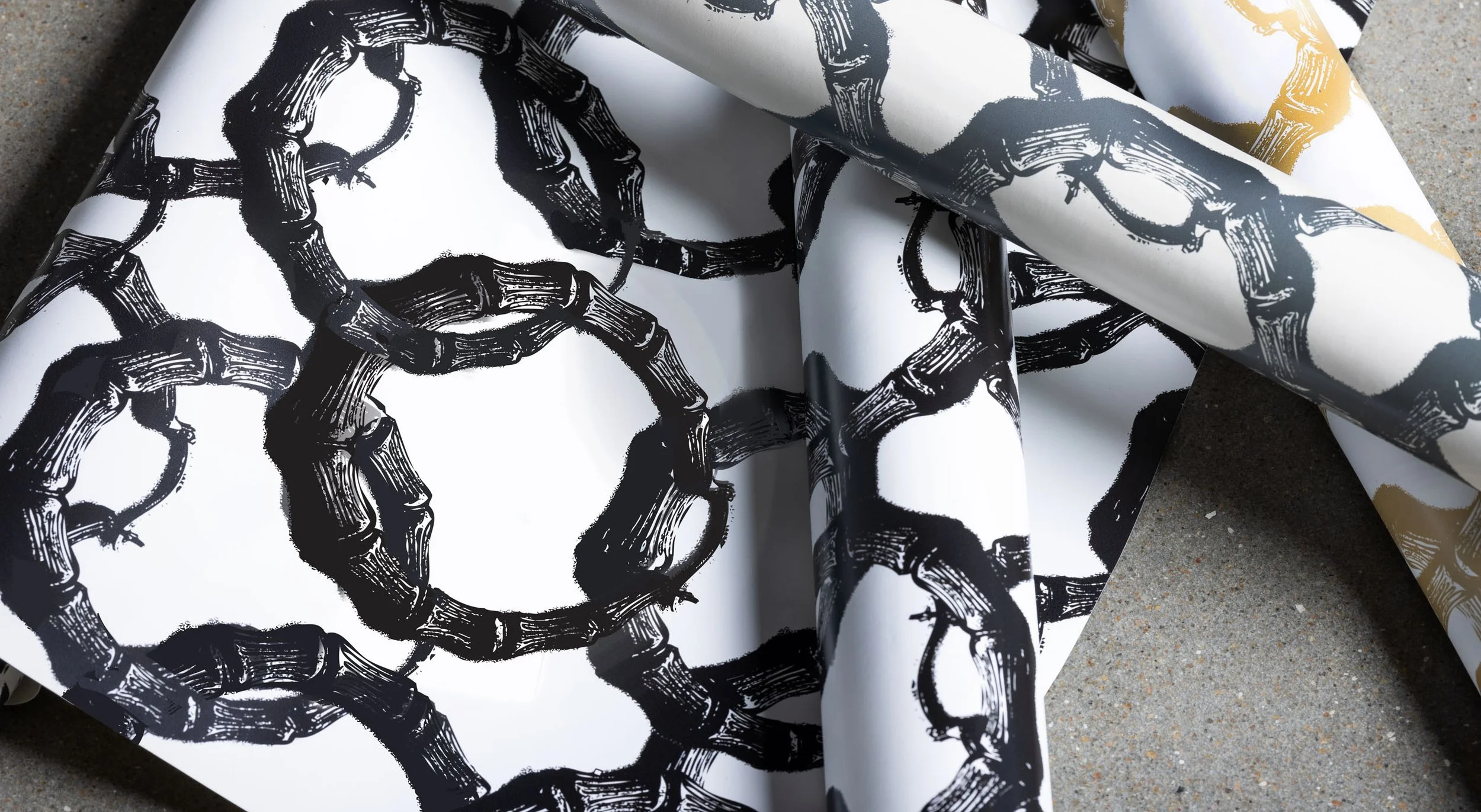 Rolled sheets of black, gray, and gold bamboo-patterned wallpaper layered on a flat surface.