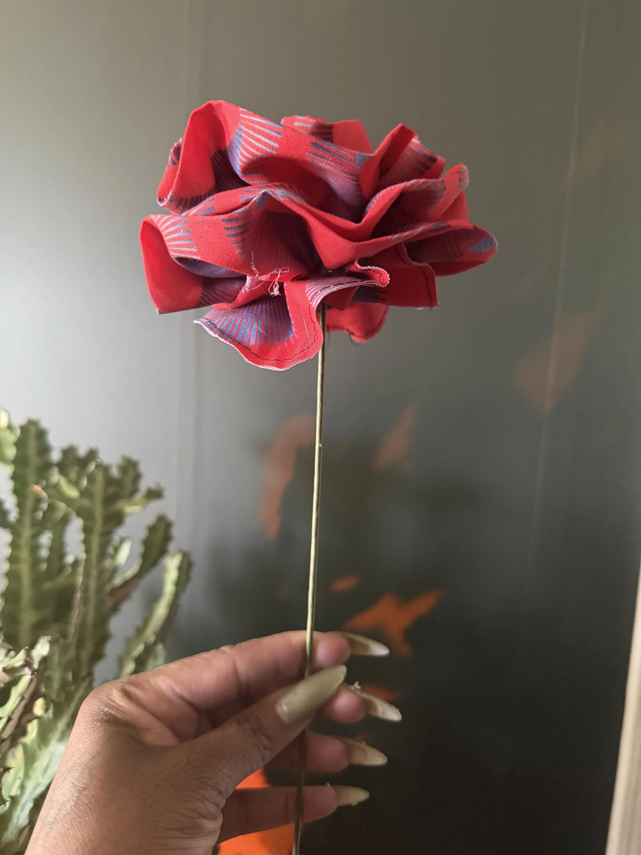 Hand holding a red handmade fabric flower on a slender stem.