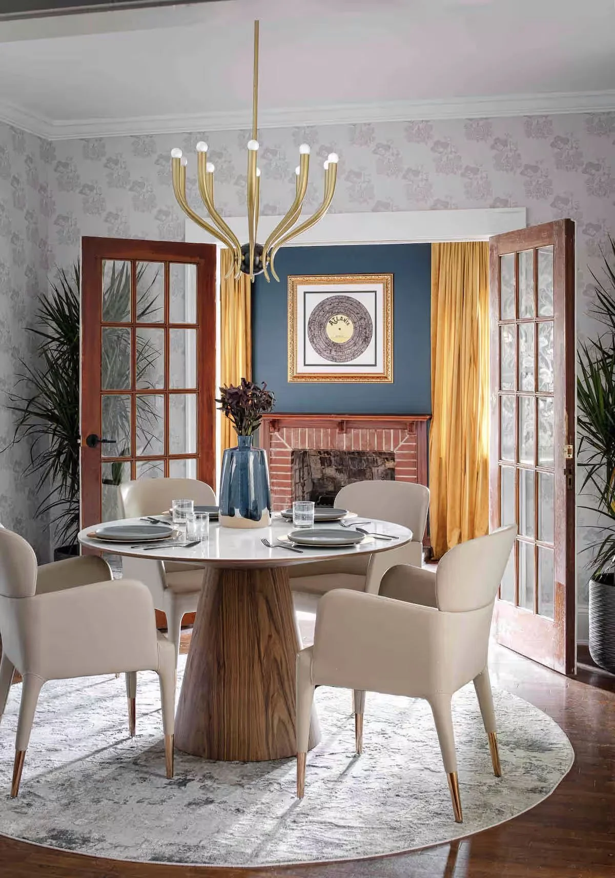 Big Boi Airbnb dining room with custom neutral wallpaper, round wood dining table, cream chairs, gold chandelier, and framed record artwork.