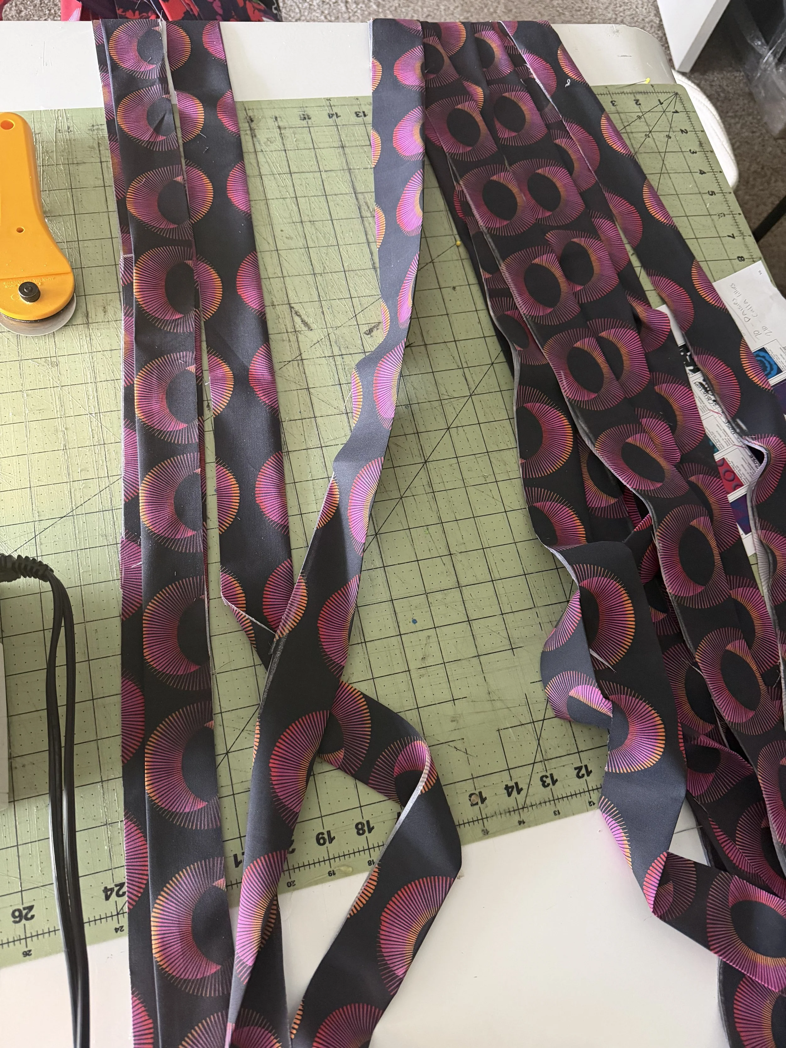 Strips of colorful patterned fabric cut on a worktable for handmade textile flowers.