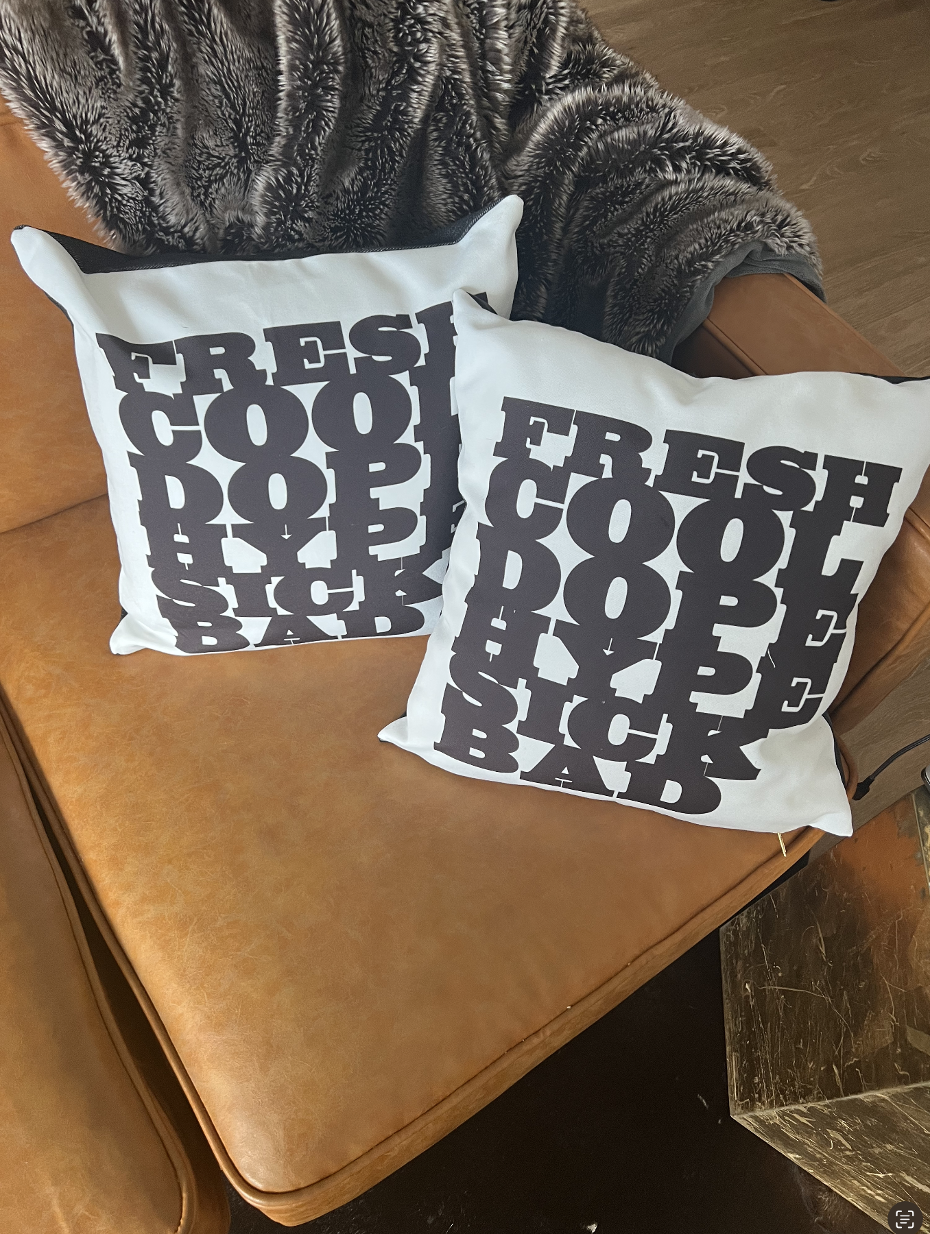 Two custom black and white graphic pillows reading “Fresh Cool Dope Black” displayed on a caramel leather sofa.
