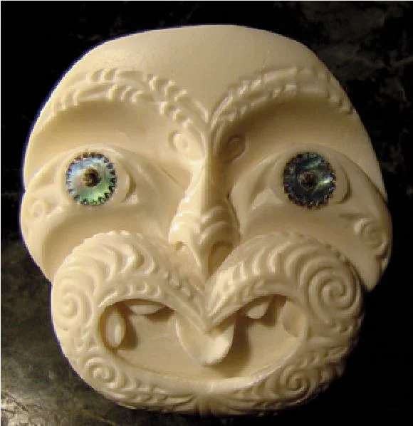A typically stylised carving of a human face showing how half of its image has a mouth which looks ‘beak-like’