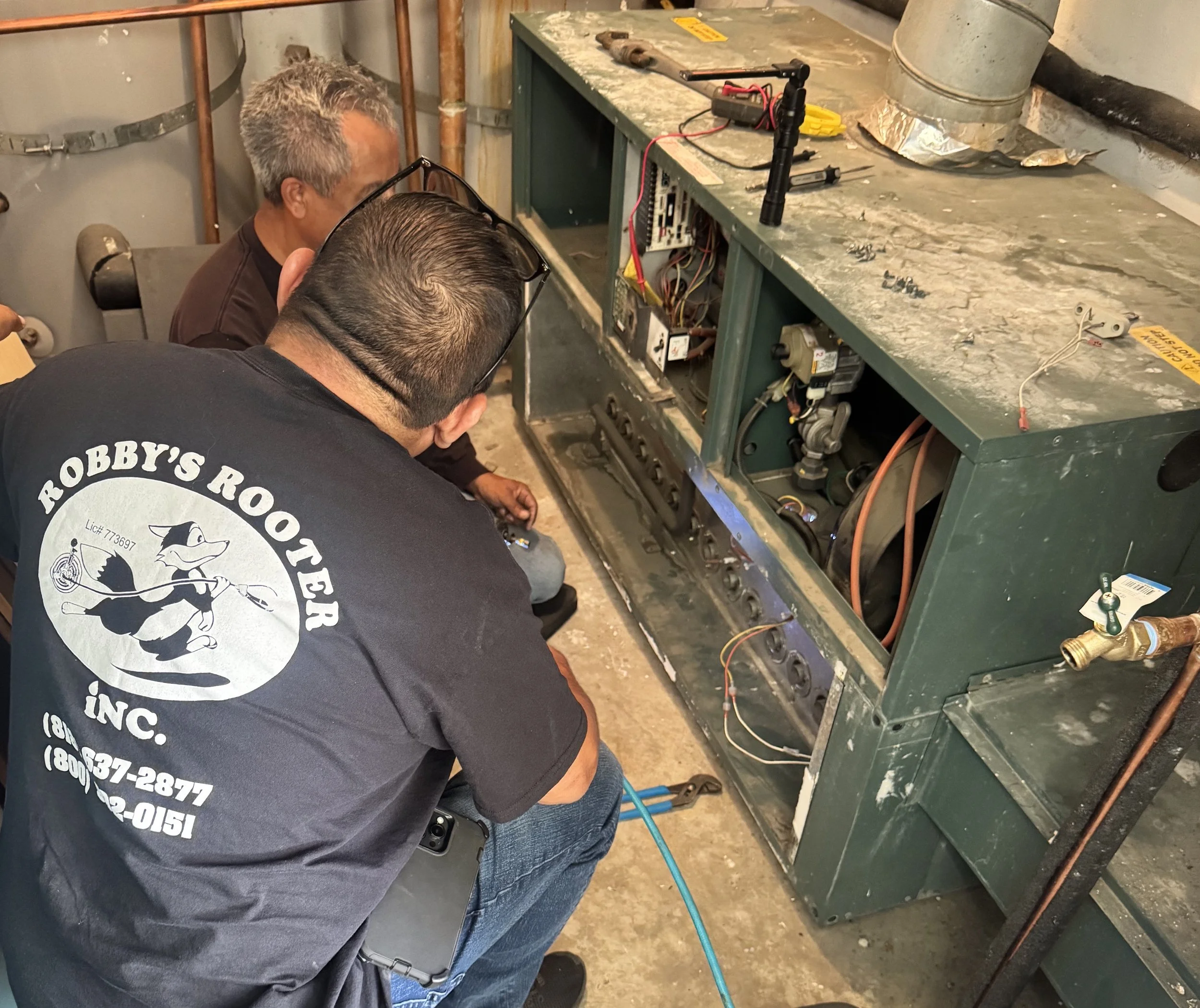 Two plumbing technicians diagnosing a failing Raypak boiler system to restore hot water at an apartment complex in Reseda, Los Angeles.