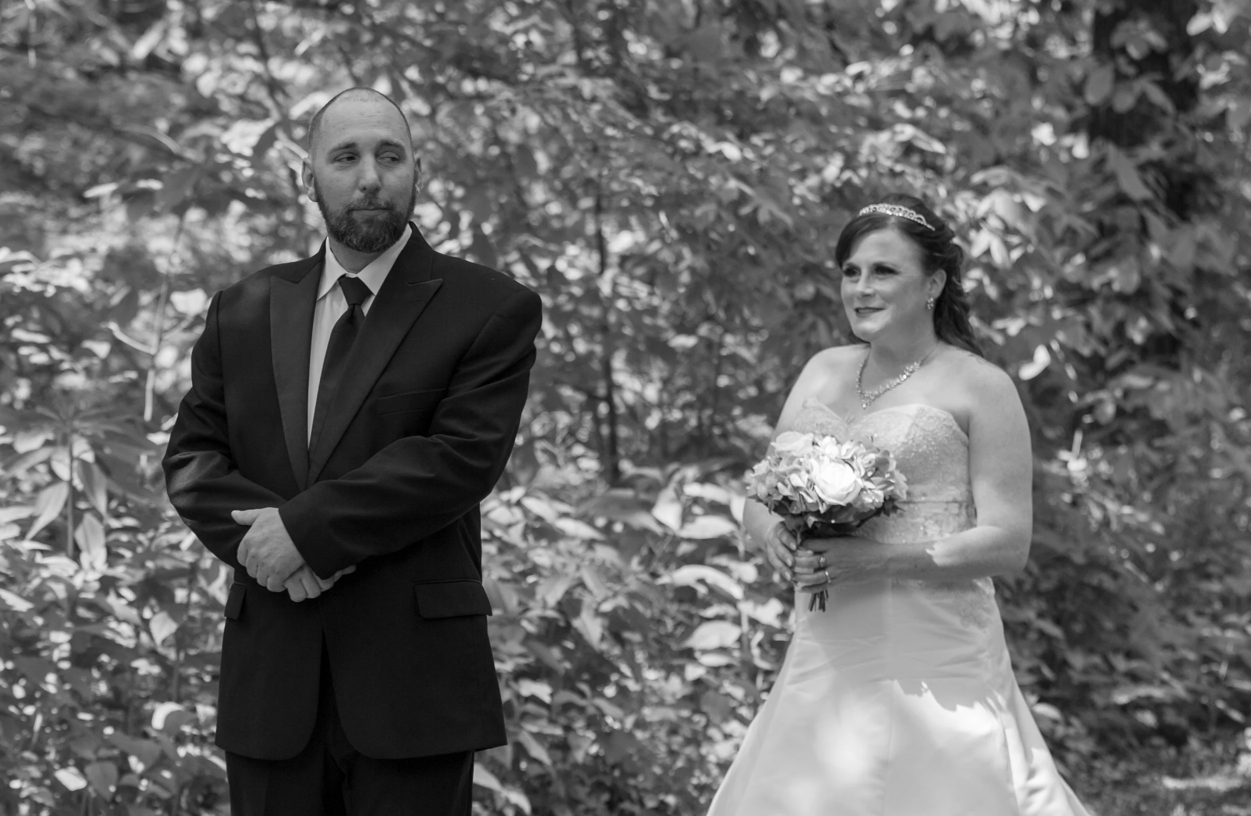 A bride and groom in formal attire during a wedding ceremony in an outdoor setting.