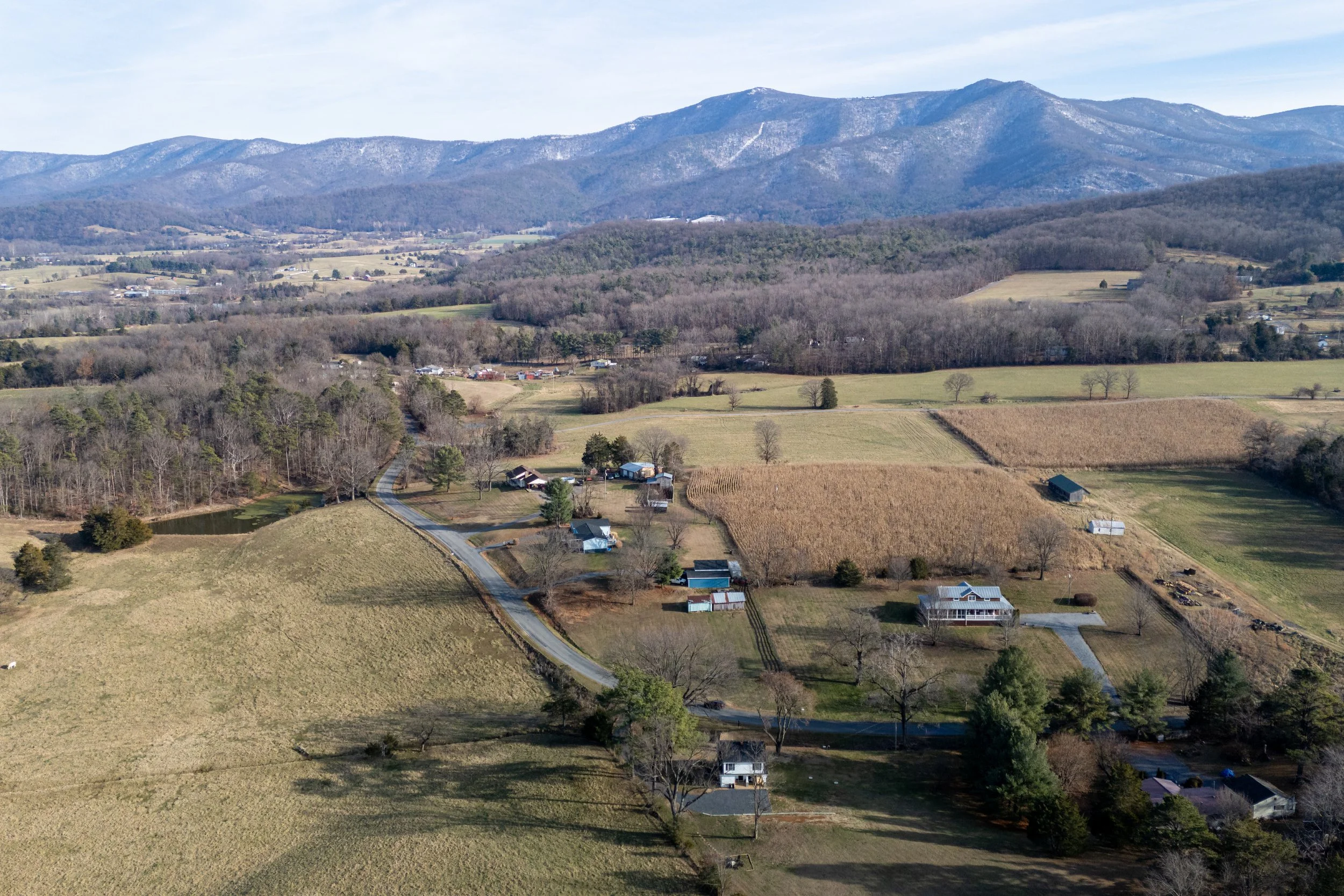A scenic landscape showing rolling hills, farmland, and distant mountains under a partly cloudy sky.