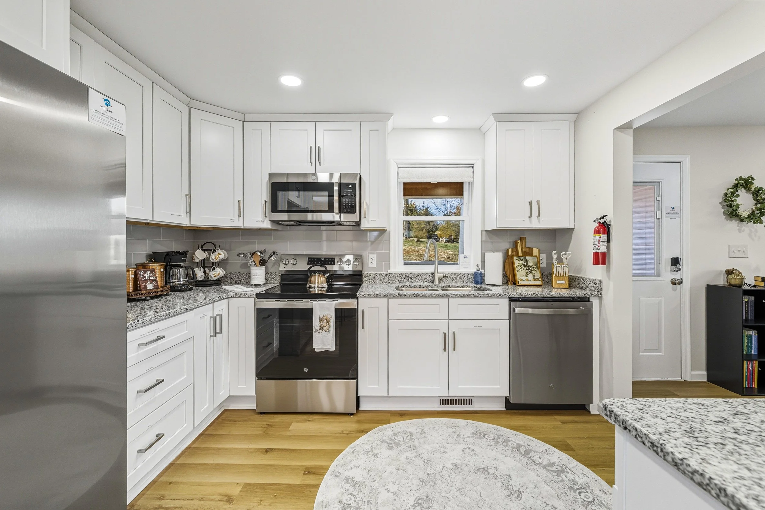 Modern kitchen with white cabinets, granite countertops, stainless steel appliances, and a window showing an outdoor scene.