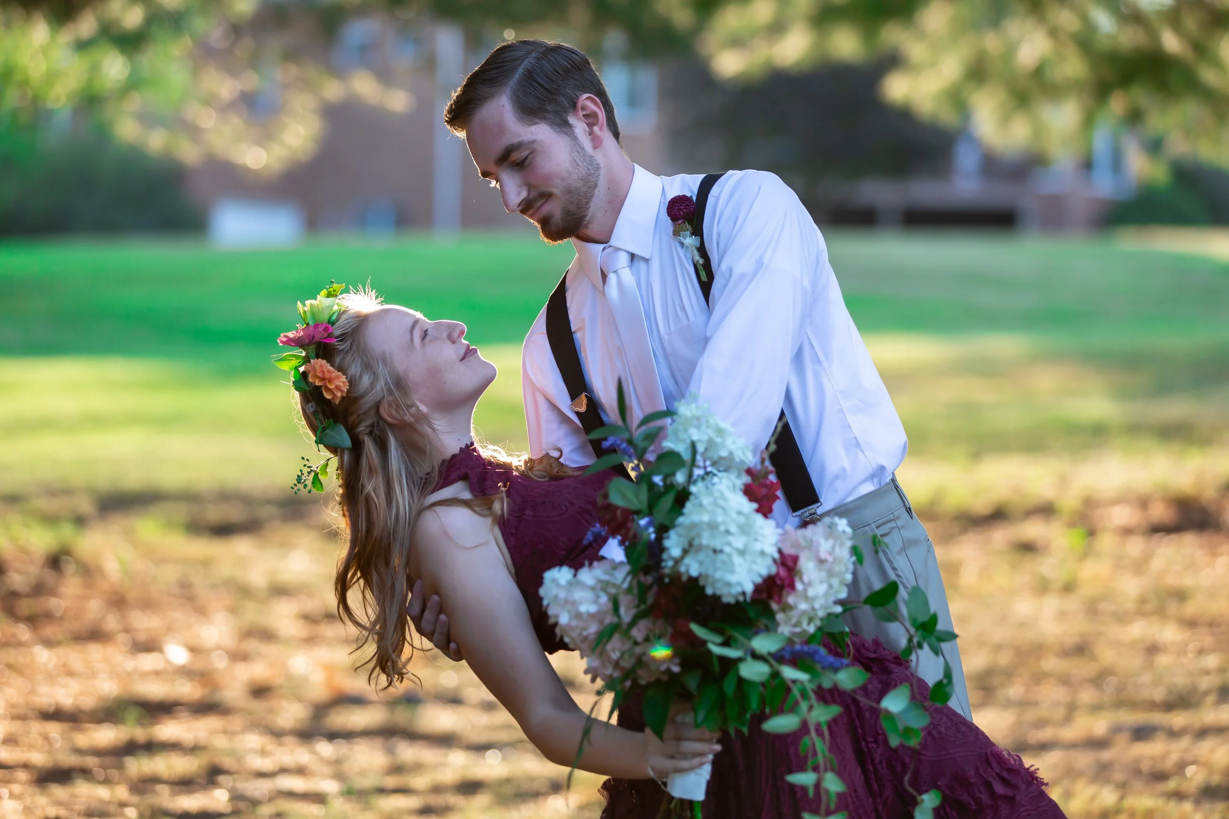 A couple in formal attire with the woman holding a bouquet, dancing in a garden setting.
