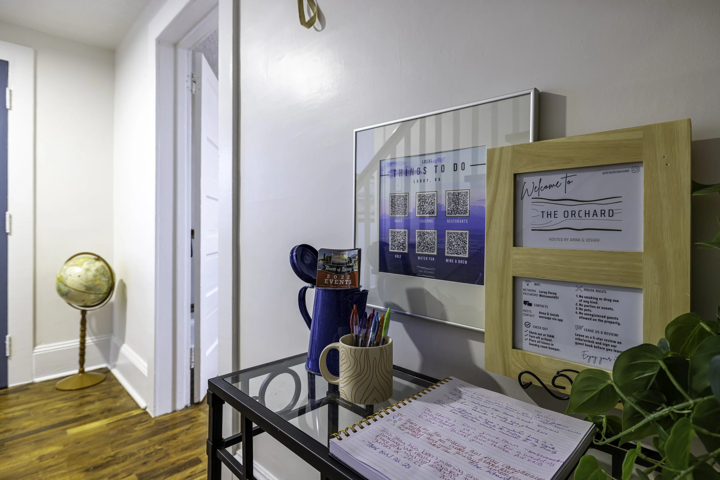 Reception area with a whiteboard, a desk with pens, a welcome sign with location details, and a globe on a stand near a hallway with wooden flooring.