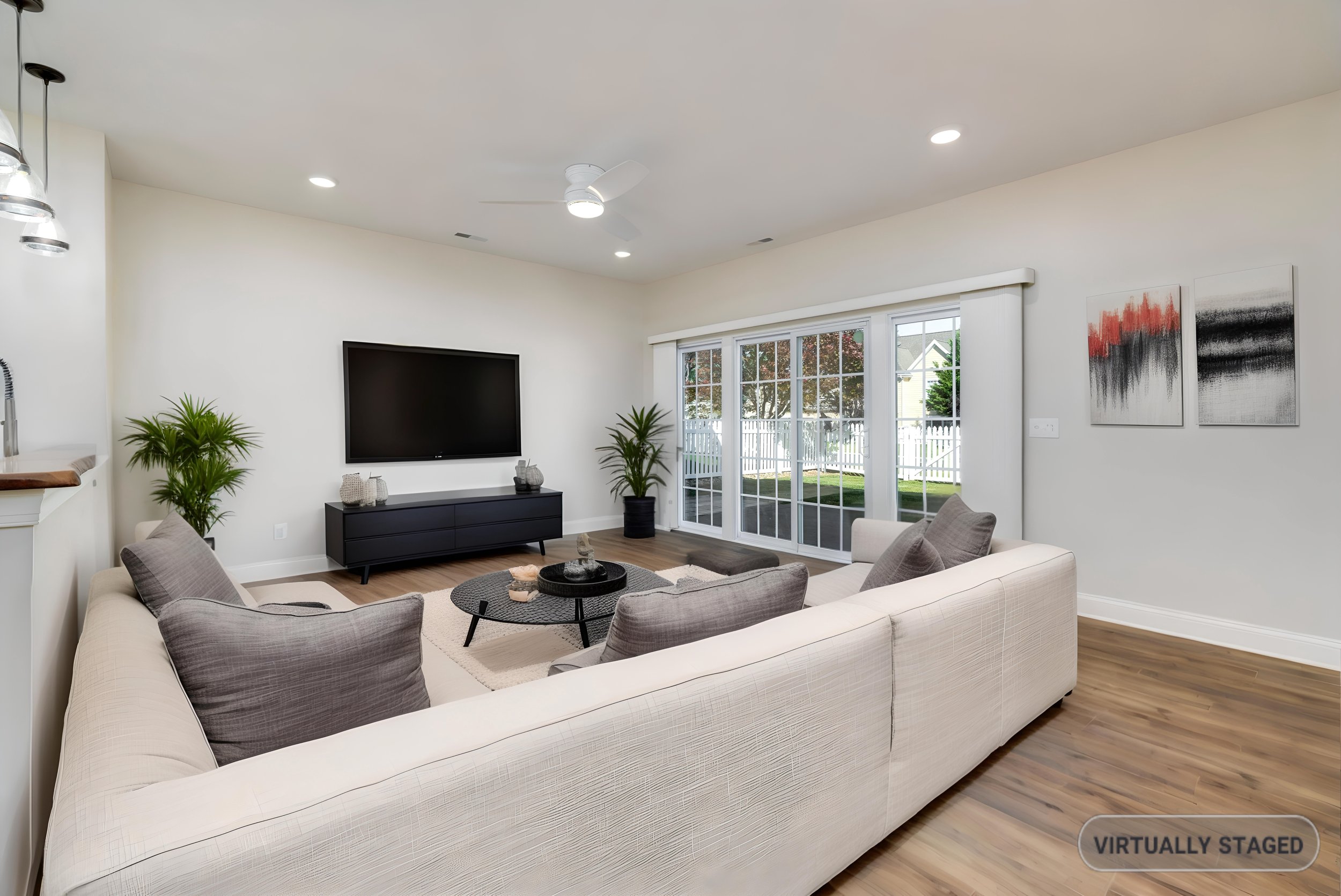 Living room with white sofa, gray armchairs, black TV stand, large window, artwork, and hardwood floors.