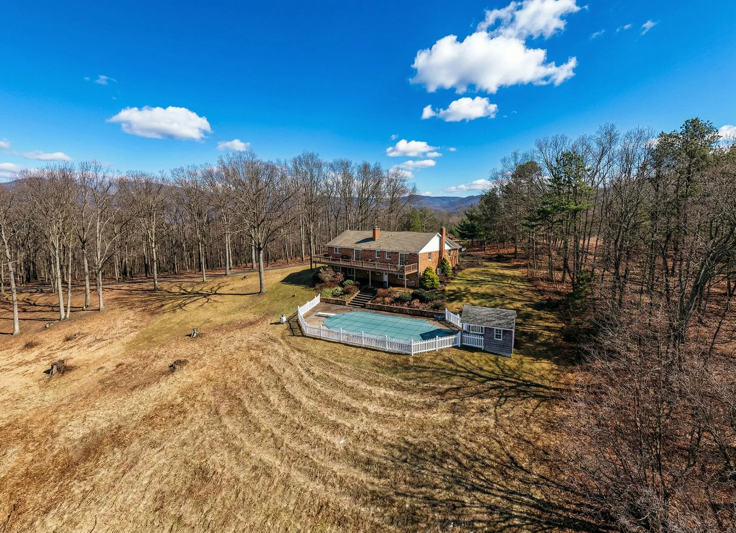 A house with a backyard surrounded by trees under a bright blue sky with scattered clouds.