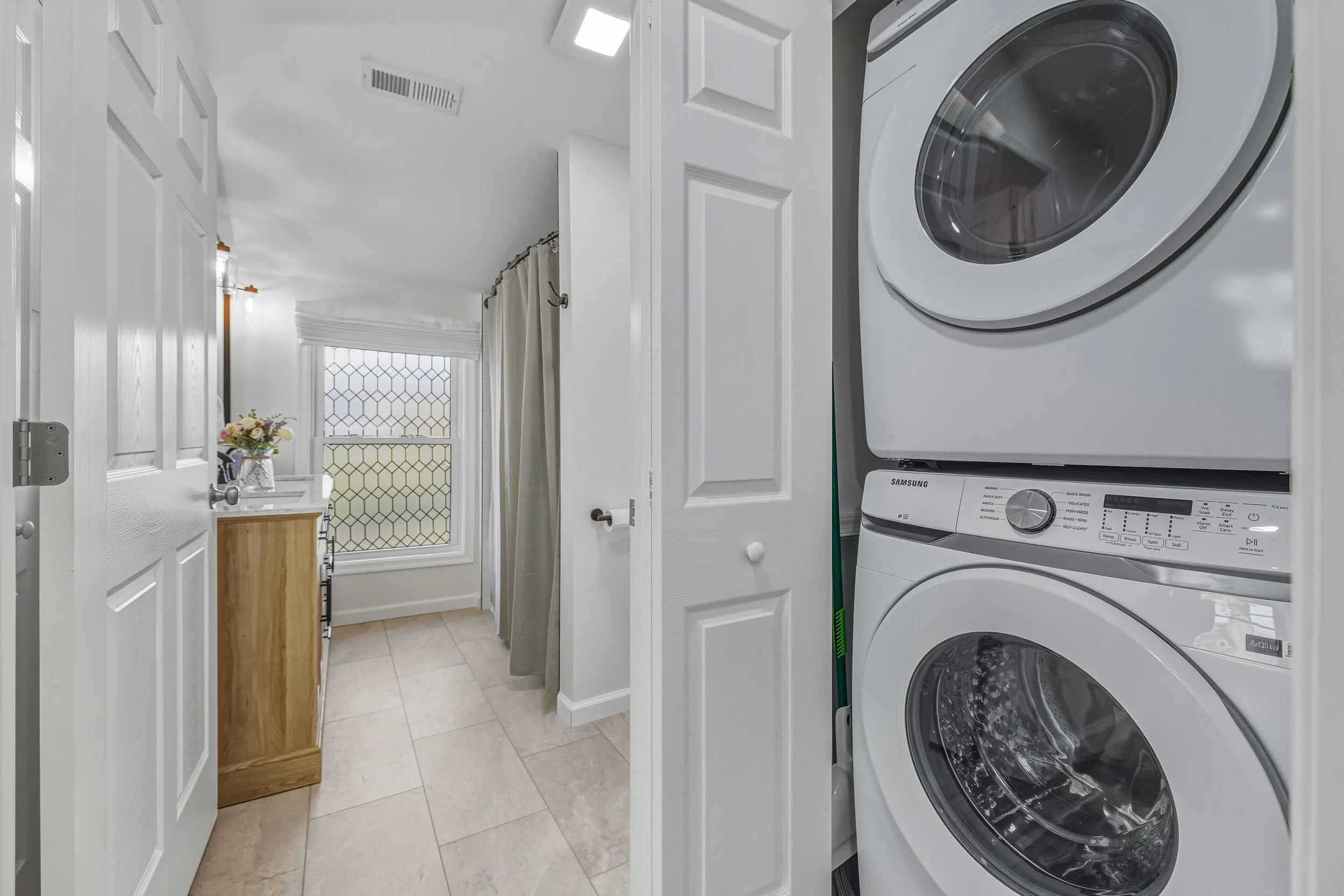 Laundry room with white washer and dryer, beige tiled floor, white walls, and a window with a diamond pattern.