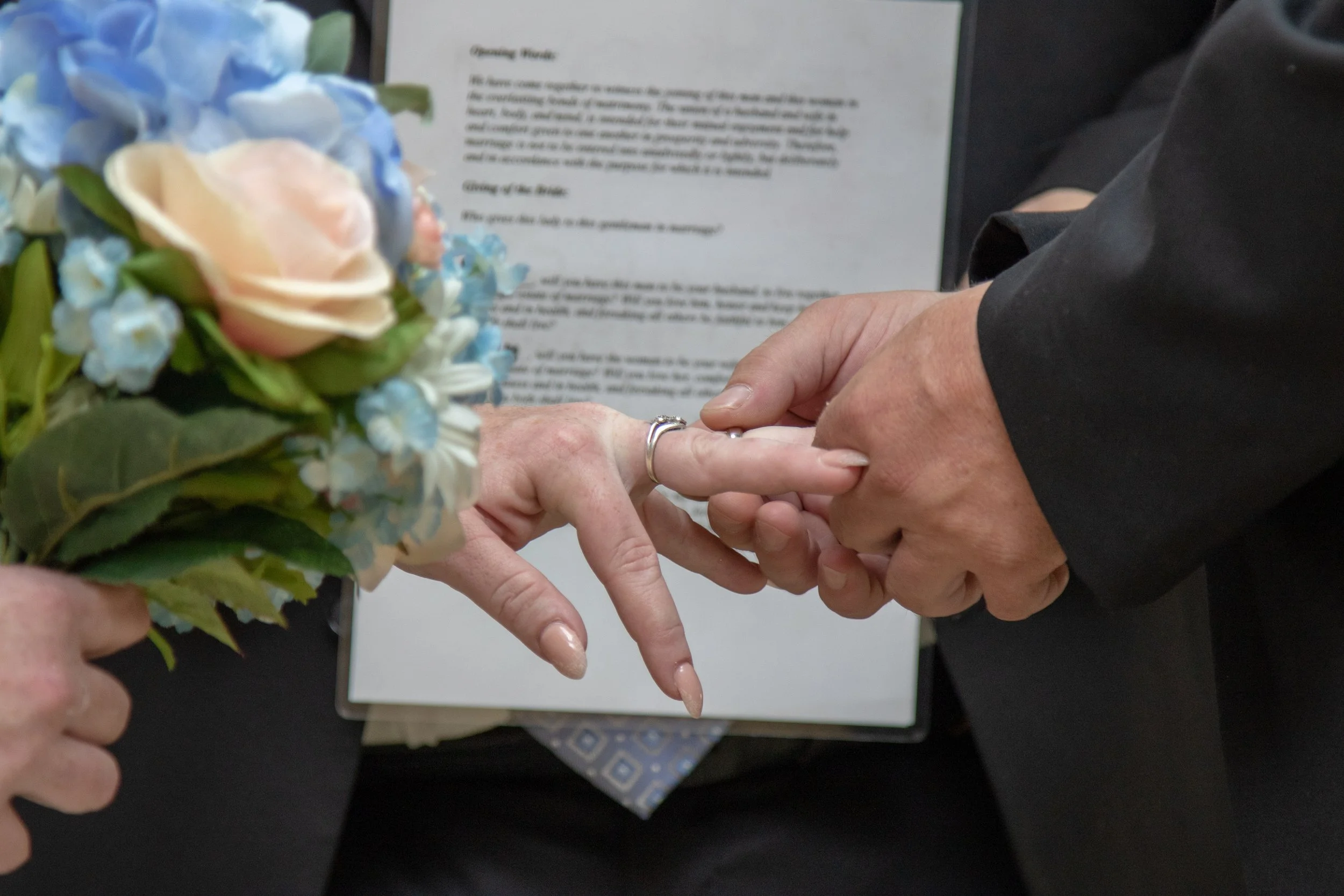 Close-up of someone holding a bouquet of flowers during a ring exchange at a wedding ceremony.