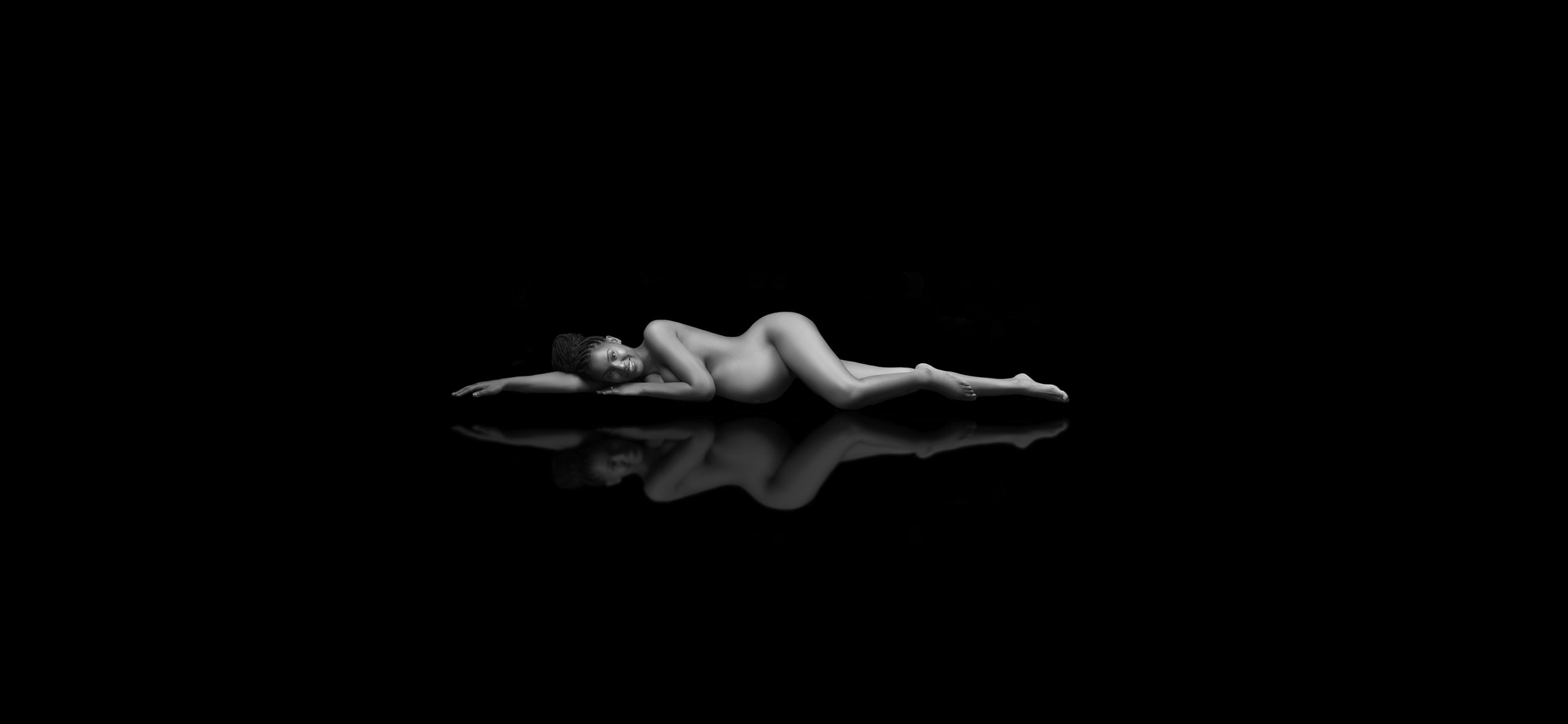 "Maternity photoshoot: Expectant mother lying on black surface with reflection on the ground