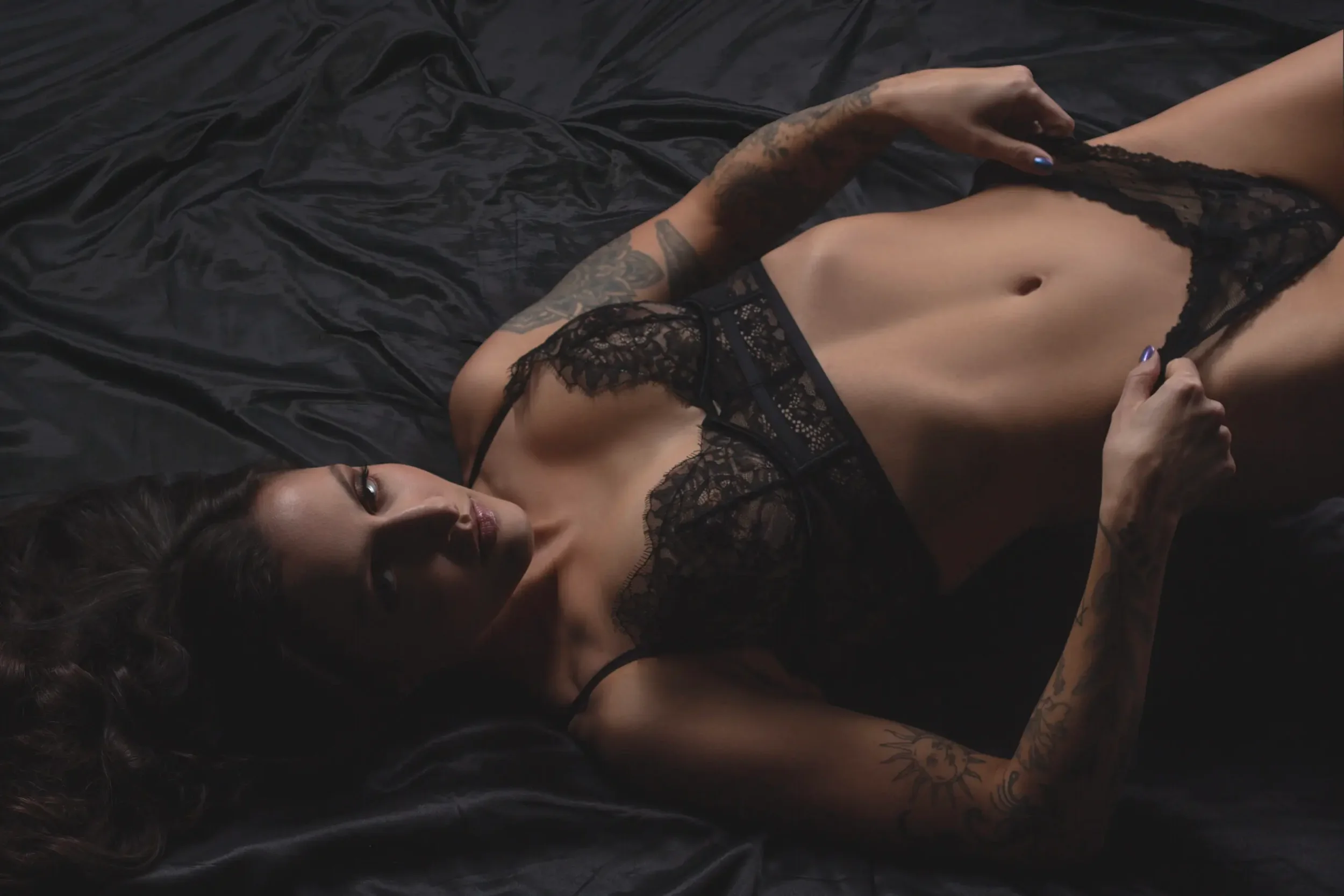 chicago-sexy-boudoir-tattooed-woman-black-lace-panties-silk-sheets.webp