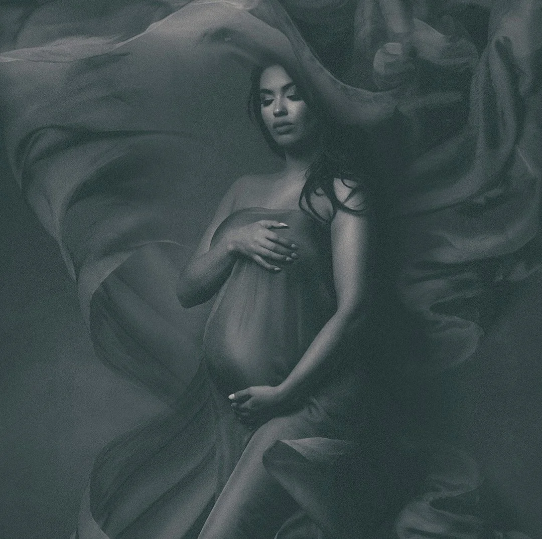 A grayscale photo of a Chicago pregnant woman lying on fabric with her shirt pulled down, gently holding her belly with one hand and covering her breast with the other.