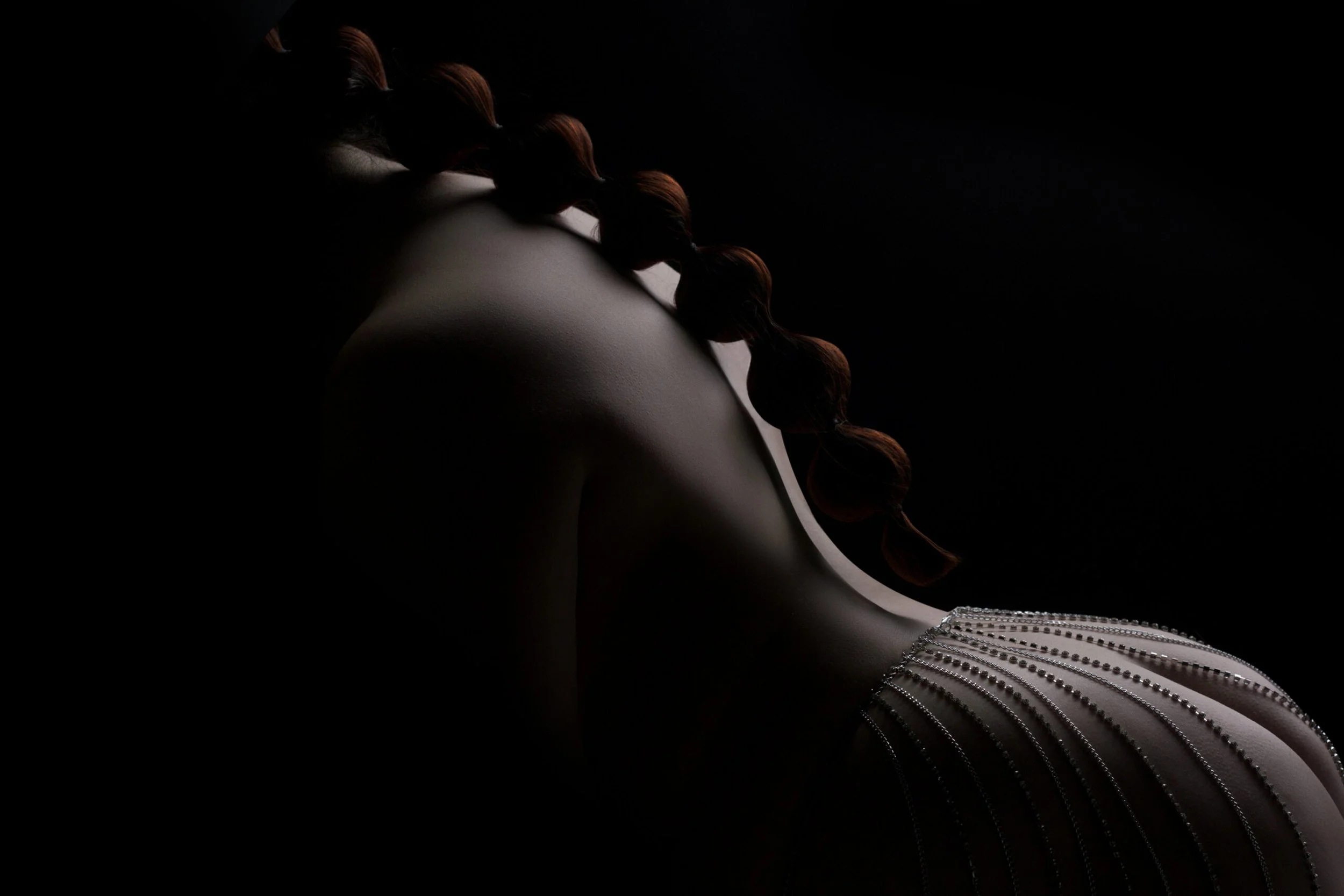 Elegant Chicago boudoir back portrait with dramatic lighting and pearl chains.