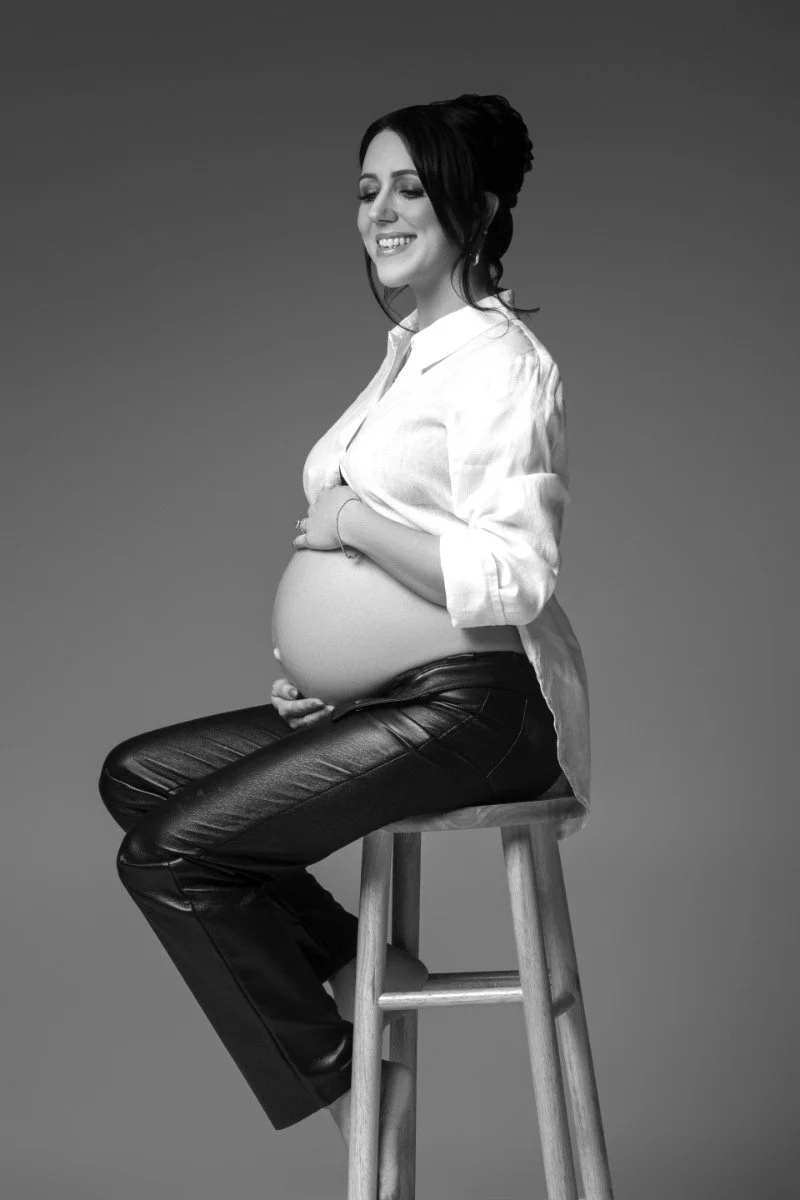 Stunning side-profile maternity portrait of a pregnant woman in elegant black lace bra and leather pants, captured in studio by Chicago maternity photographer Sri and Jana Photography