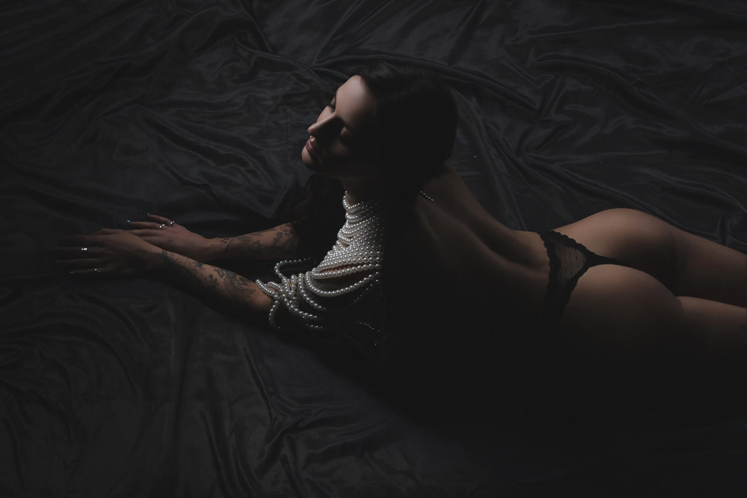 Sensual Chicago boudoir session wearing Lacey lingerie on black satin with pearl necklace.
